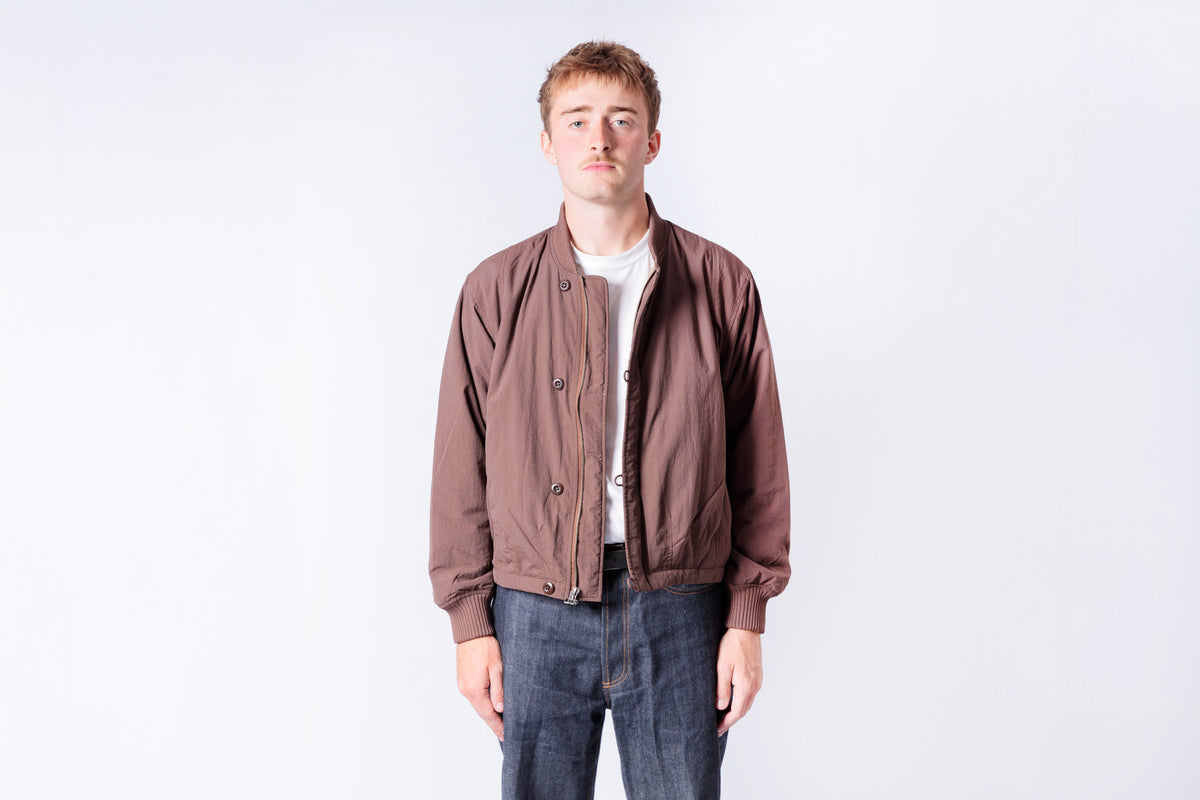 Man wearing a brown jacket and dark jeans on a white background