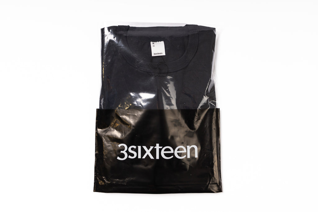 Black t-shirt in a clear plastic bag with '3sixteen' branding on a white background