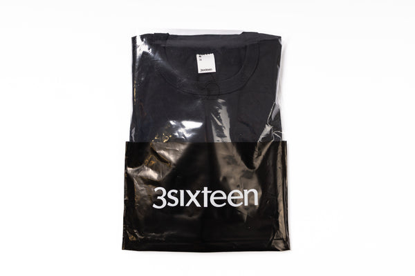 Black t-shirt in a clear plastic bag with '3sixteen' branding on a white background