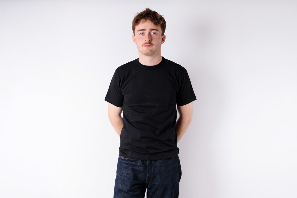 Person wearing a black t-shirt and dark jeans against a white background