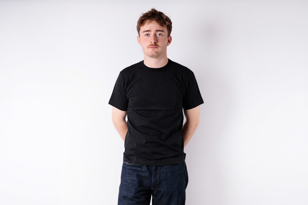Person wearing a black t-shirt and dark jeans against a white background
