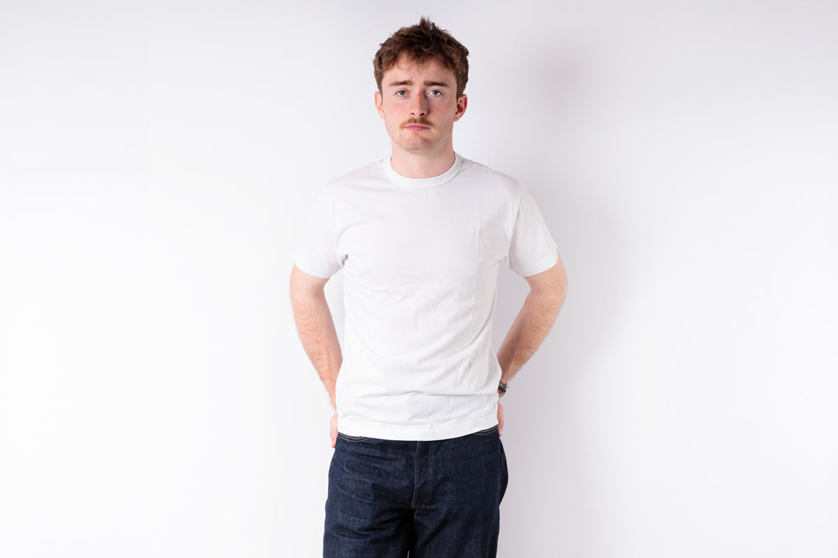 Person wearing a white t-shirt and dark pants on a plain background