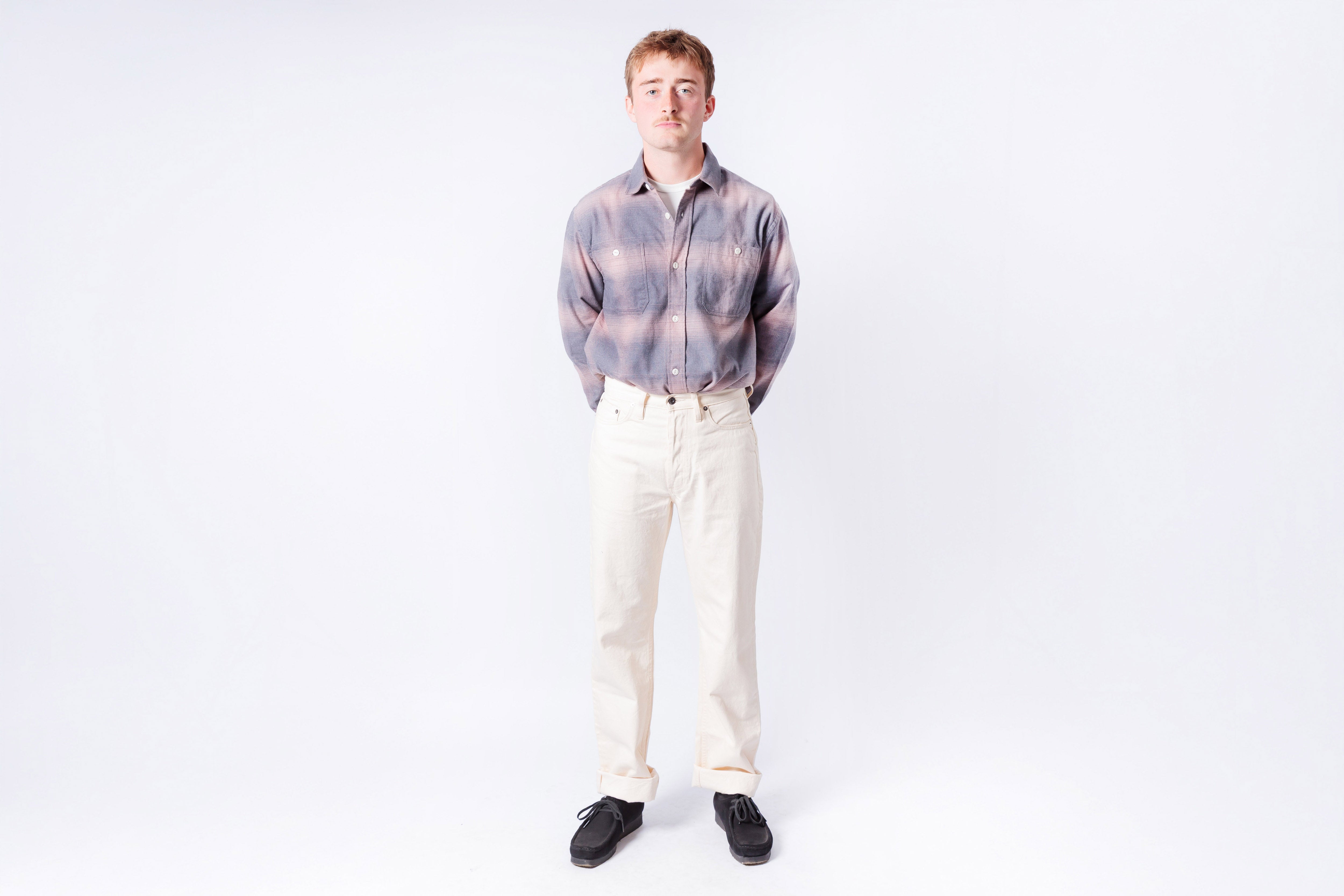 Man wearing a plaid shirt and white pants on a white background