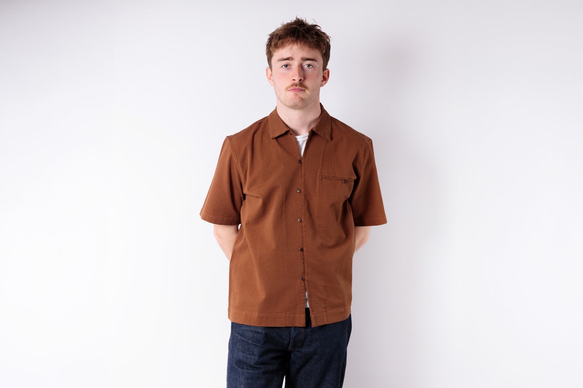 Man wearing a brown shirt and dark pants against a white background