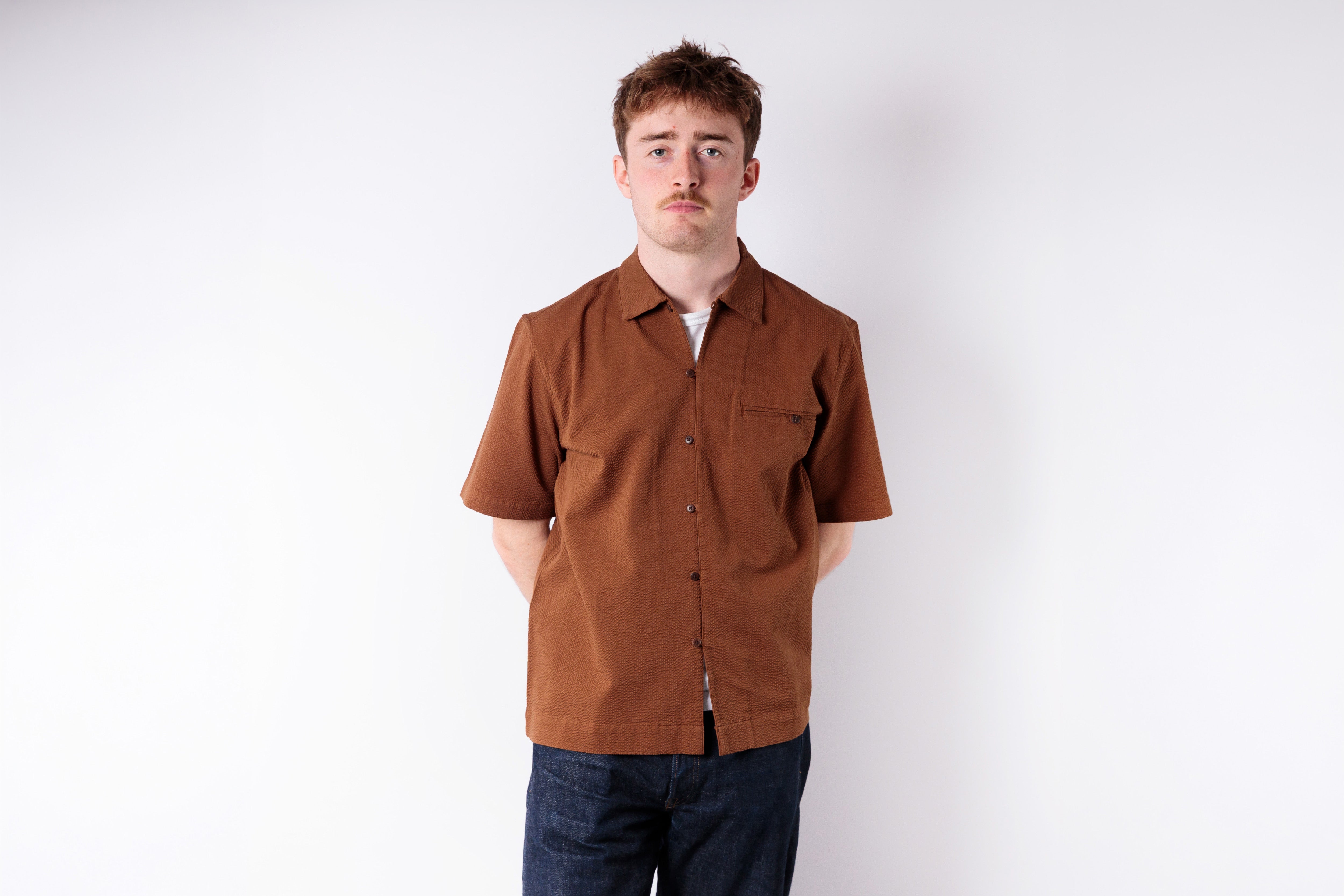 Man wearing a brown shirt and dark pants against a white background