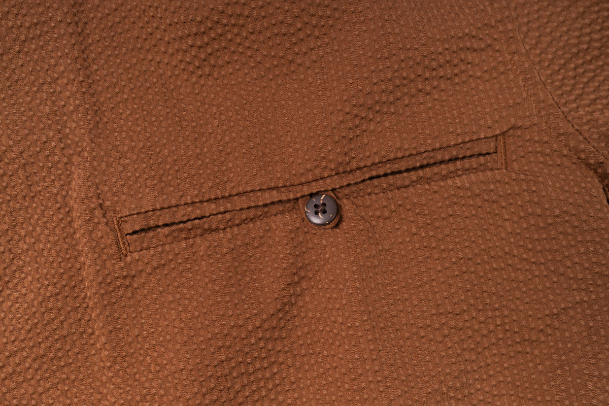 Close-up of a brown textured fabric with a button on a pocket.