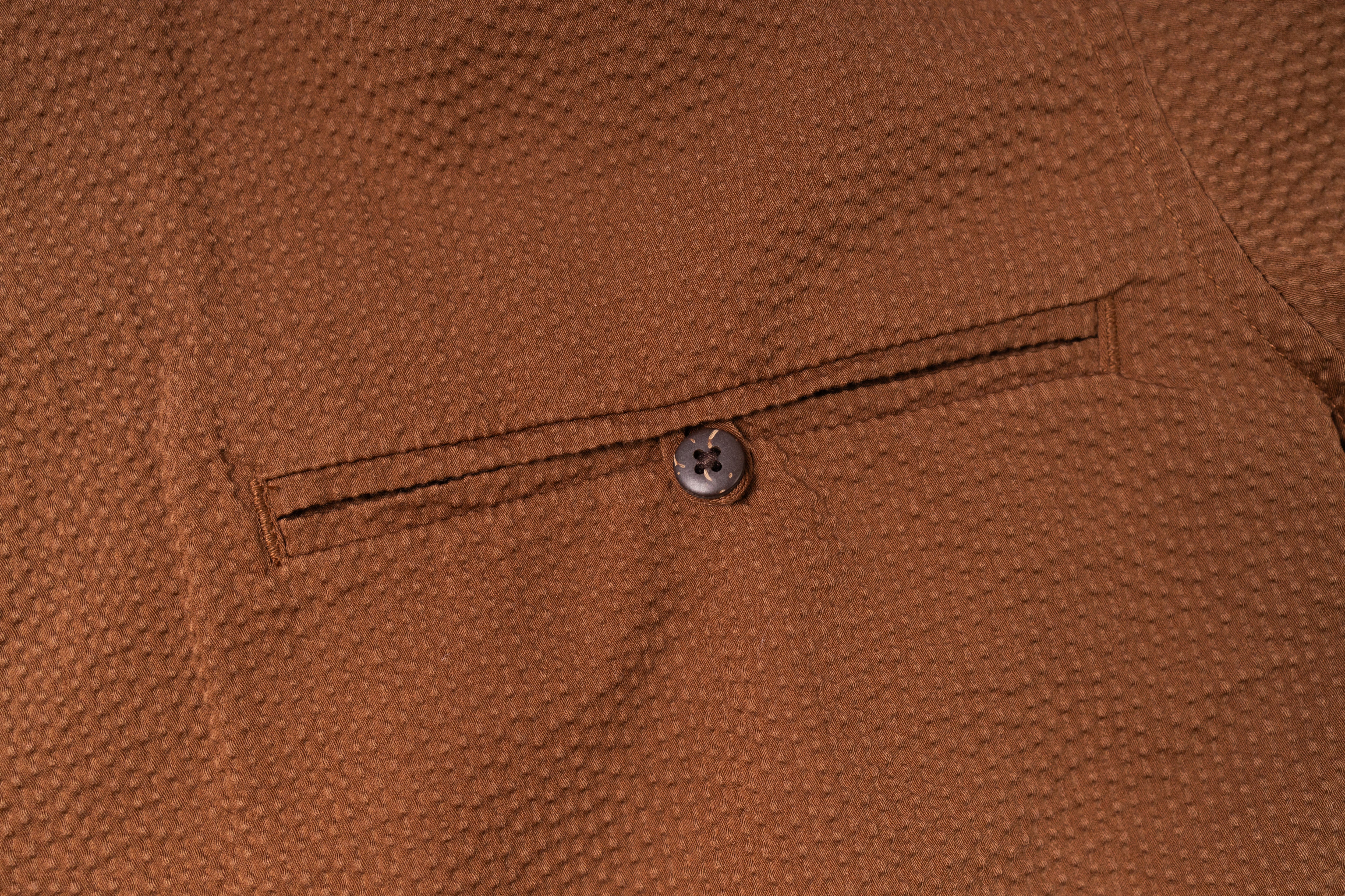 Close-up of a brown textured fabric with a button on a pocket.