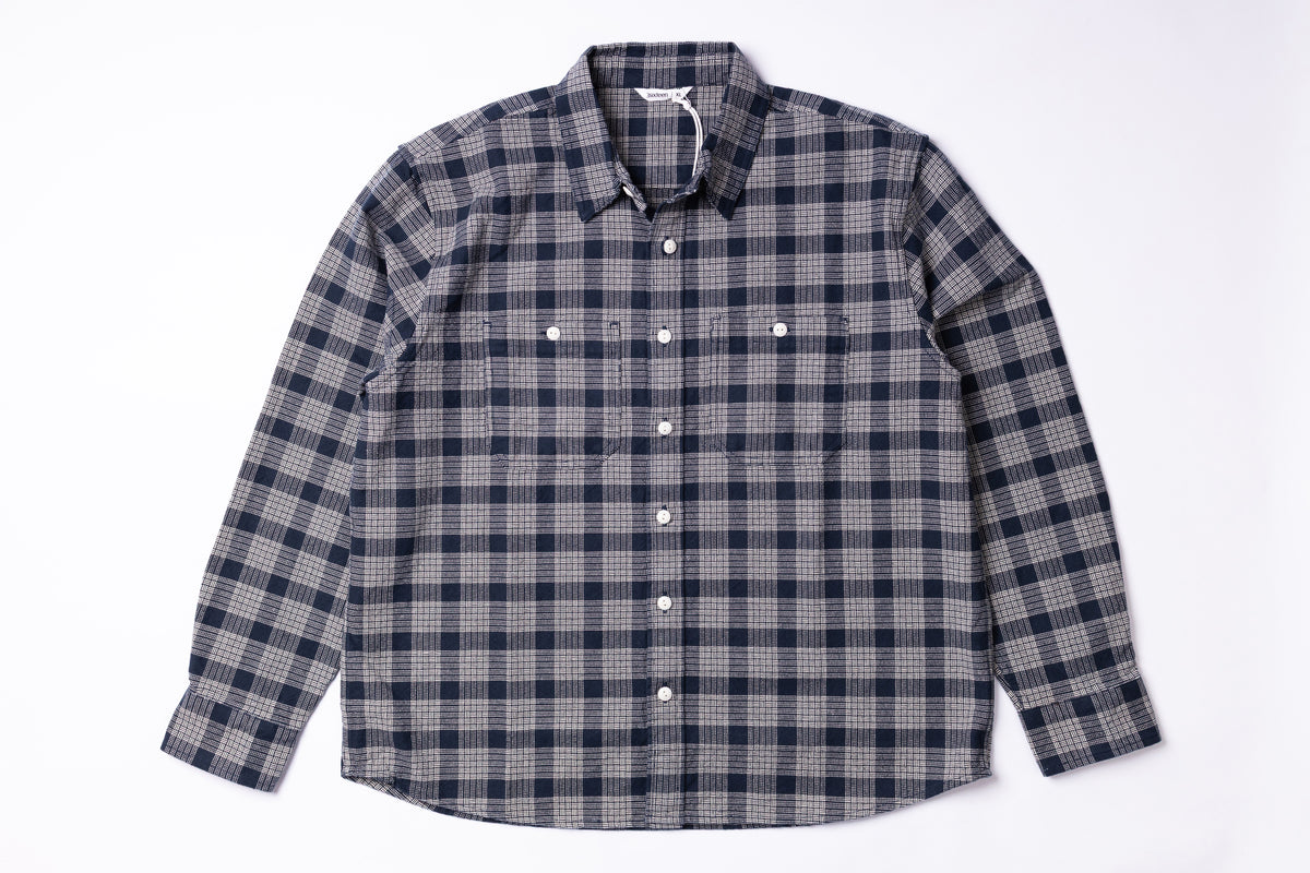 A long-sleeve button-up shirt with a navy, gray, and white plaid pattern, laid flat against a white background.