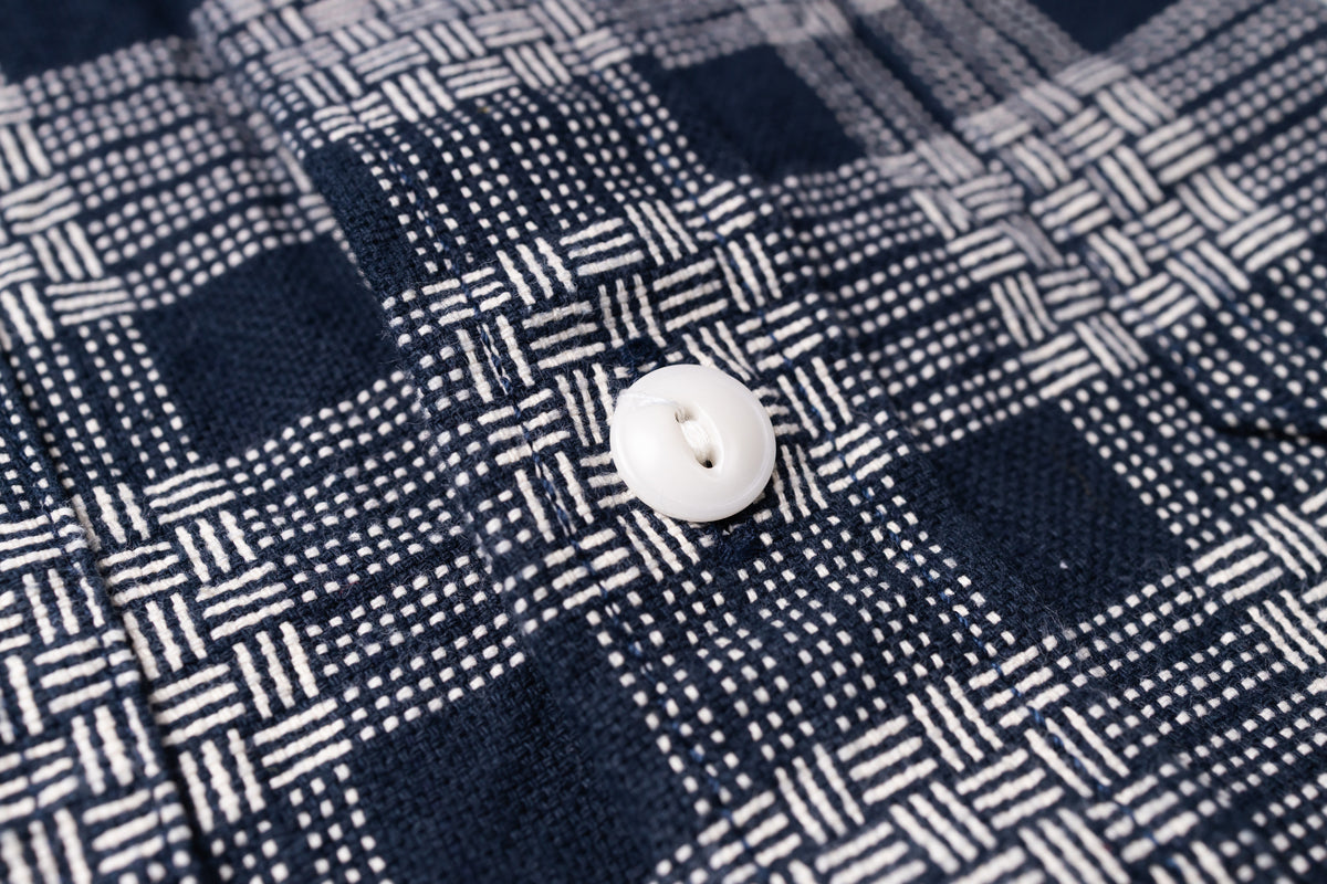 Close-up of a woven button-up shirt fabric with a navy and white plaid pattern and a single white button.