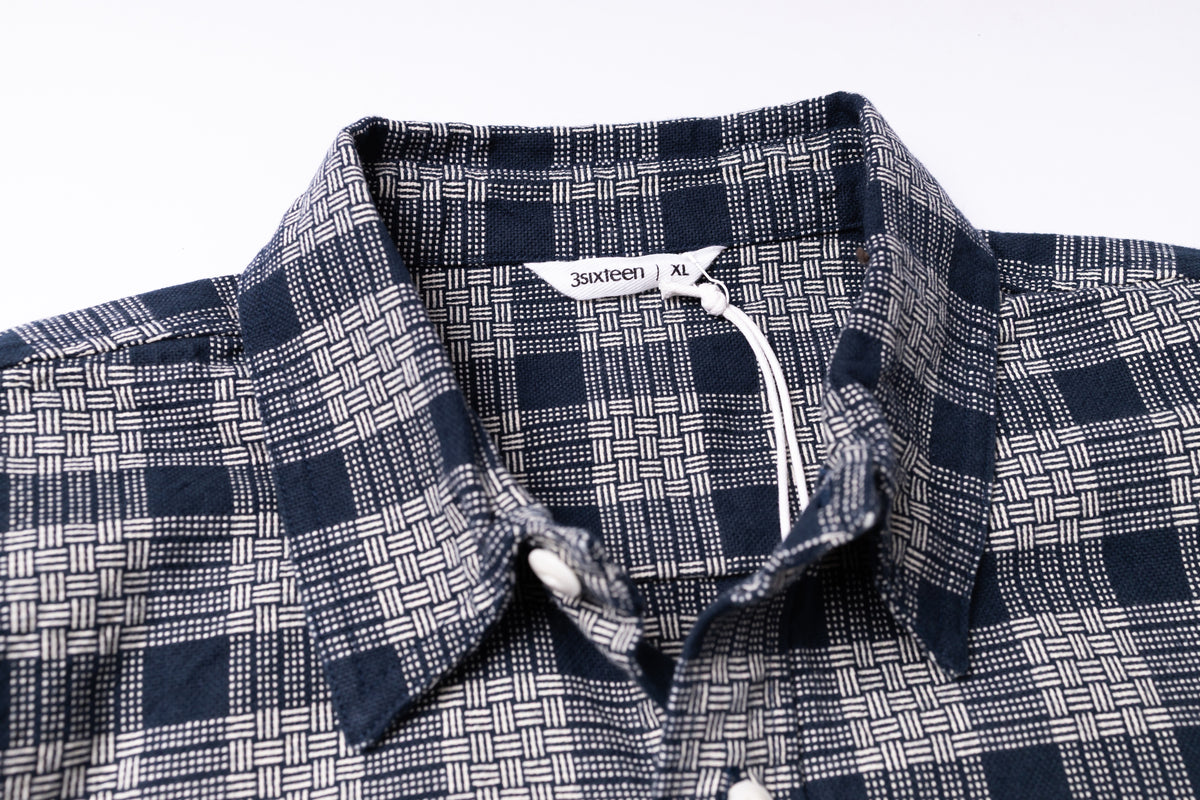 Close-up of a collared button-up shirt with a navy and white basketweave plaid pattern.