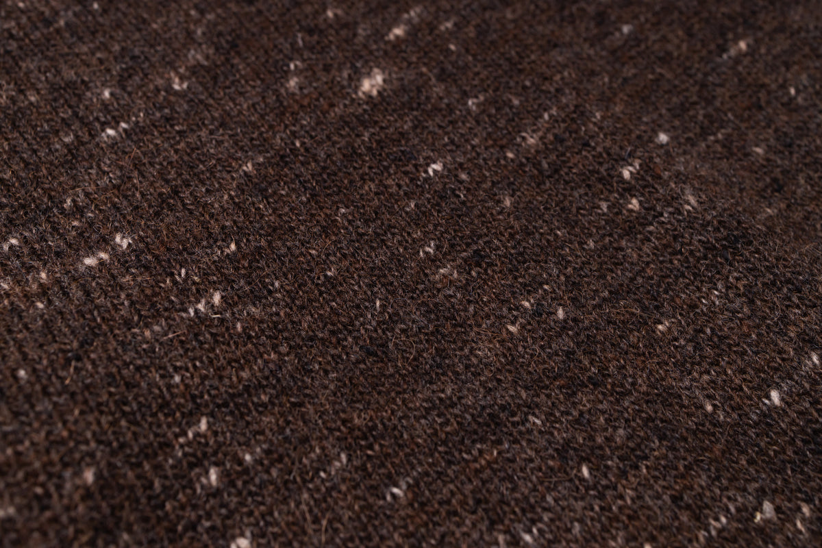 A close-up of a dark brown knit fabric with small white and beige flecks throughout.