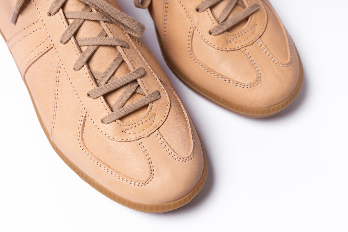 A pair of tan leather sneakers with matching laces, shown in a close-up studio shot on a white background.