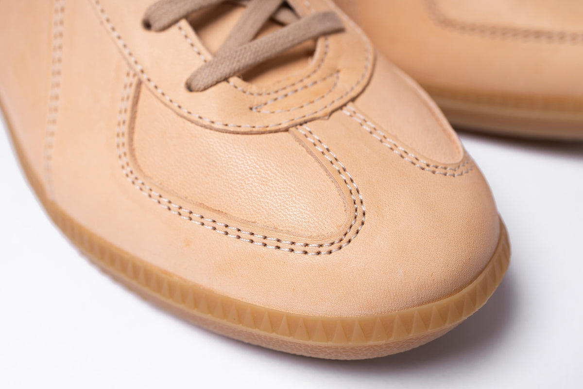 Close-up of a tan leather sneaker showing the toe cap, laces, and gum sole on a white background.