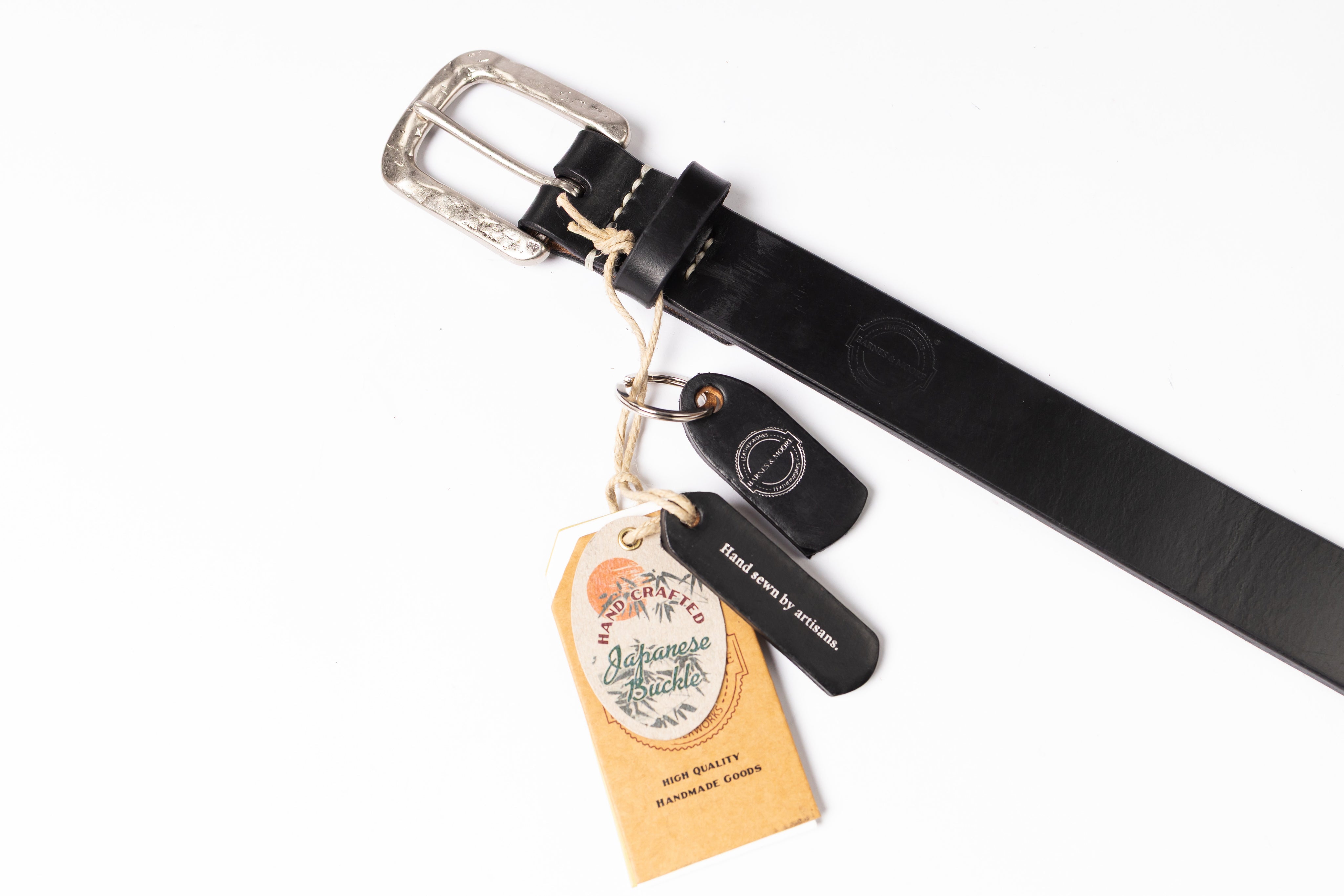 A black leather belt with a silver-toned buckle, shown on a white background with attached paper tags and a small black leather tag.