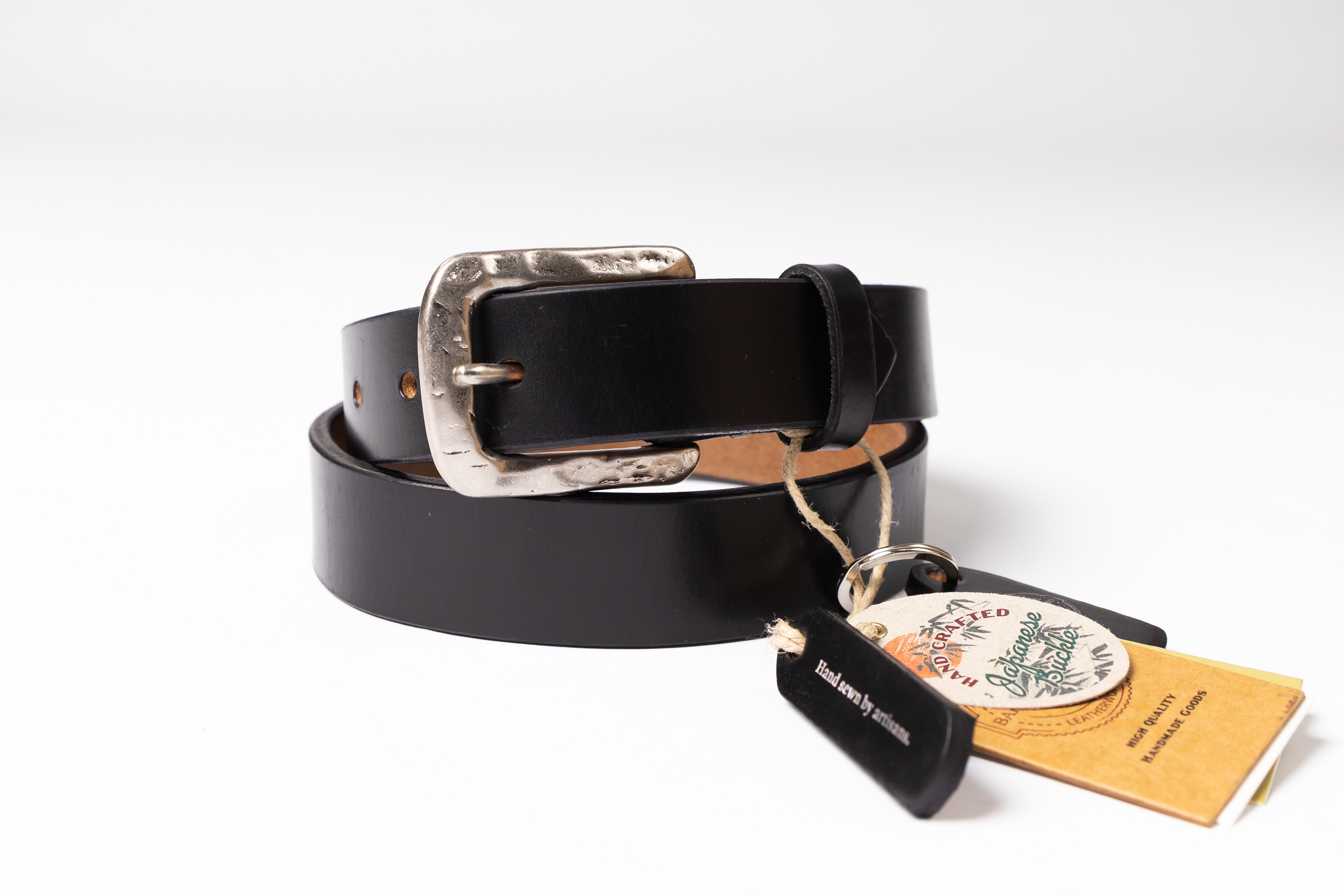 A black leather belt with a hammered silver-tone metal buckle, coiled on a white background with its original paper tags attached.