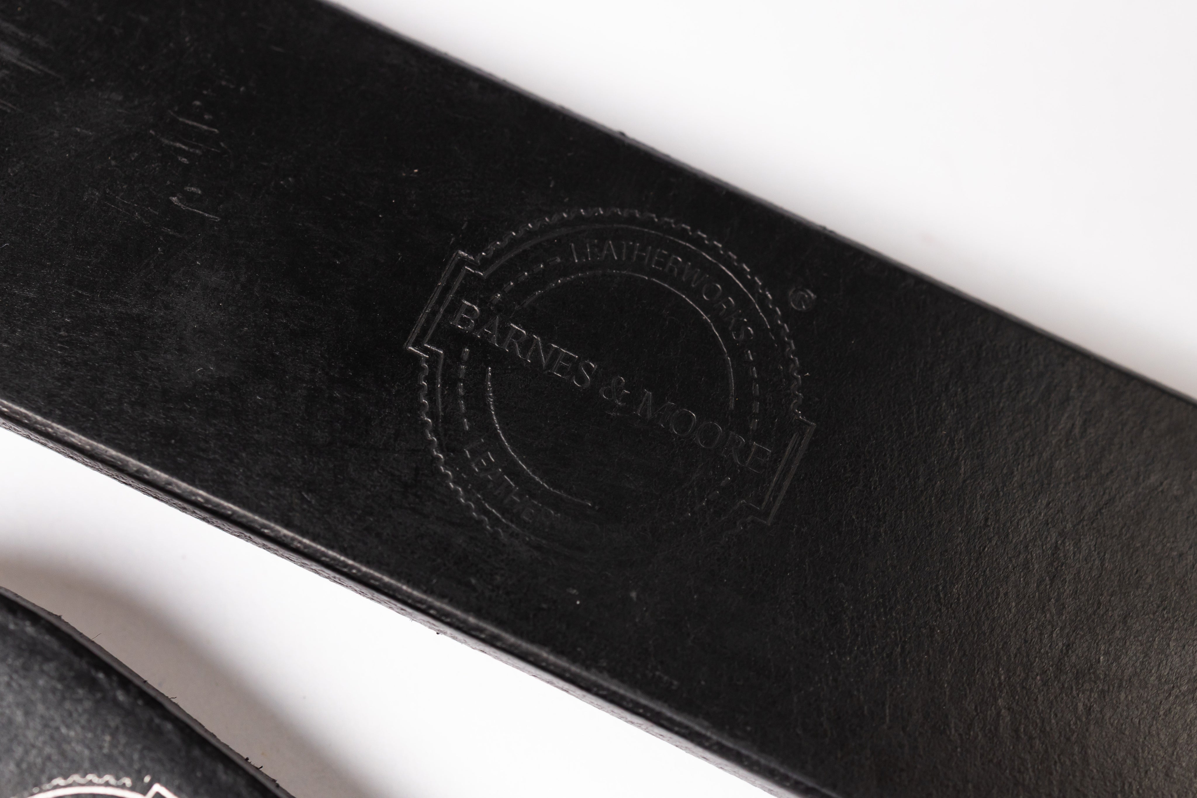 Close-up of a black leather strap with an embossed circular logo reading 'Barnes & Noble Leather Goods' on a white background.