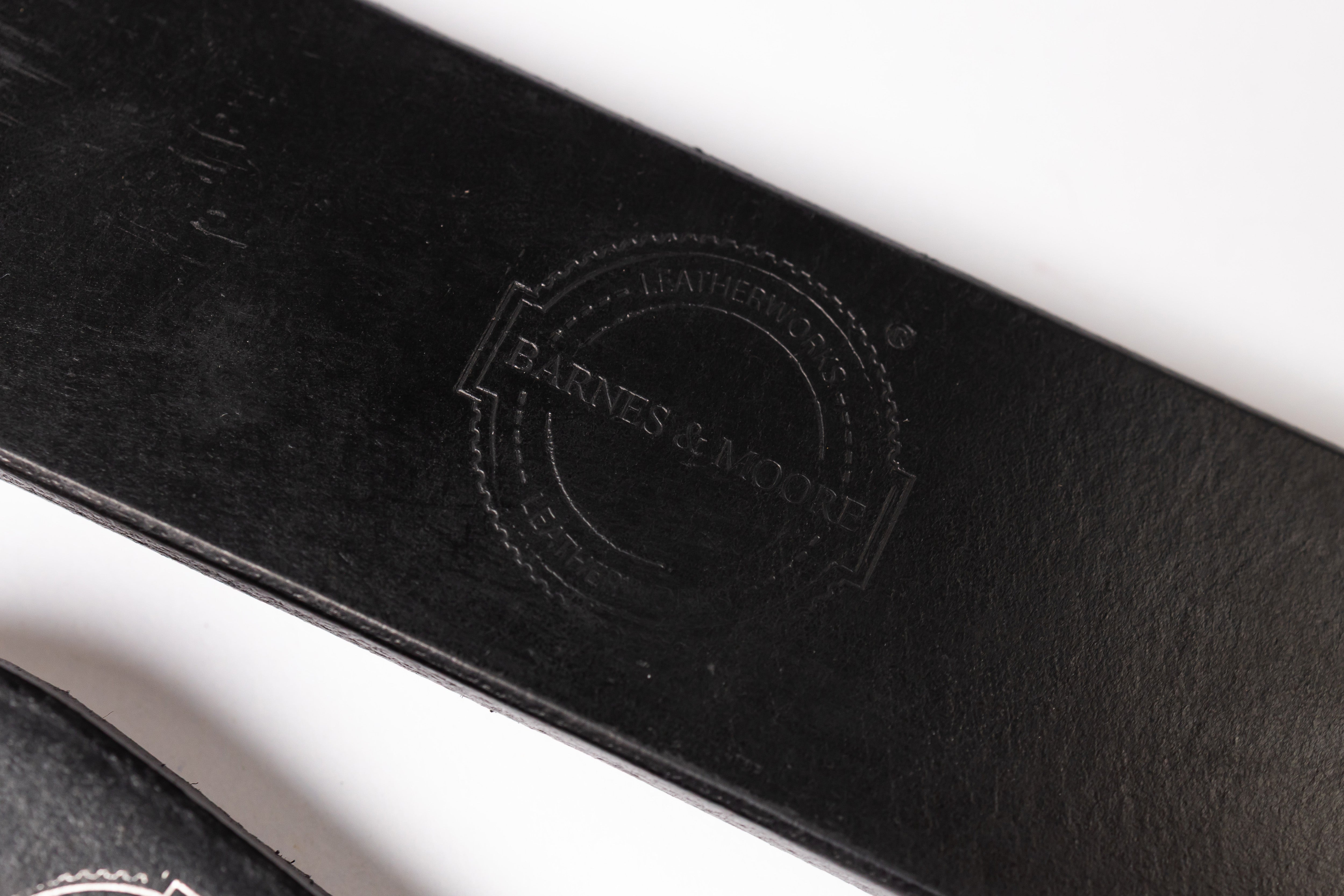 Close-up of a black leather strap with an embossed circular logo reading 'Barnes & Noble Leather Goods' on a white background.
