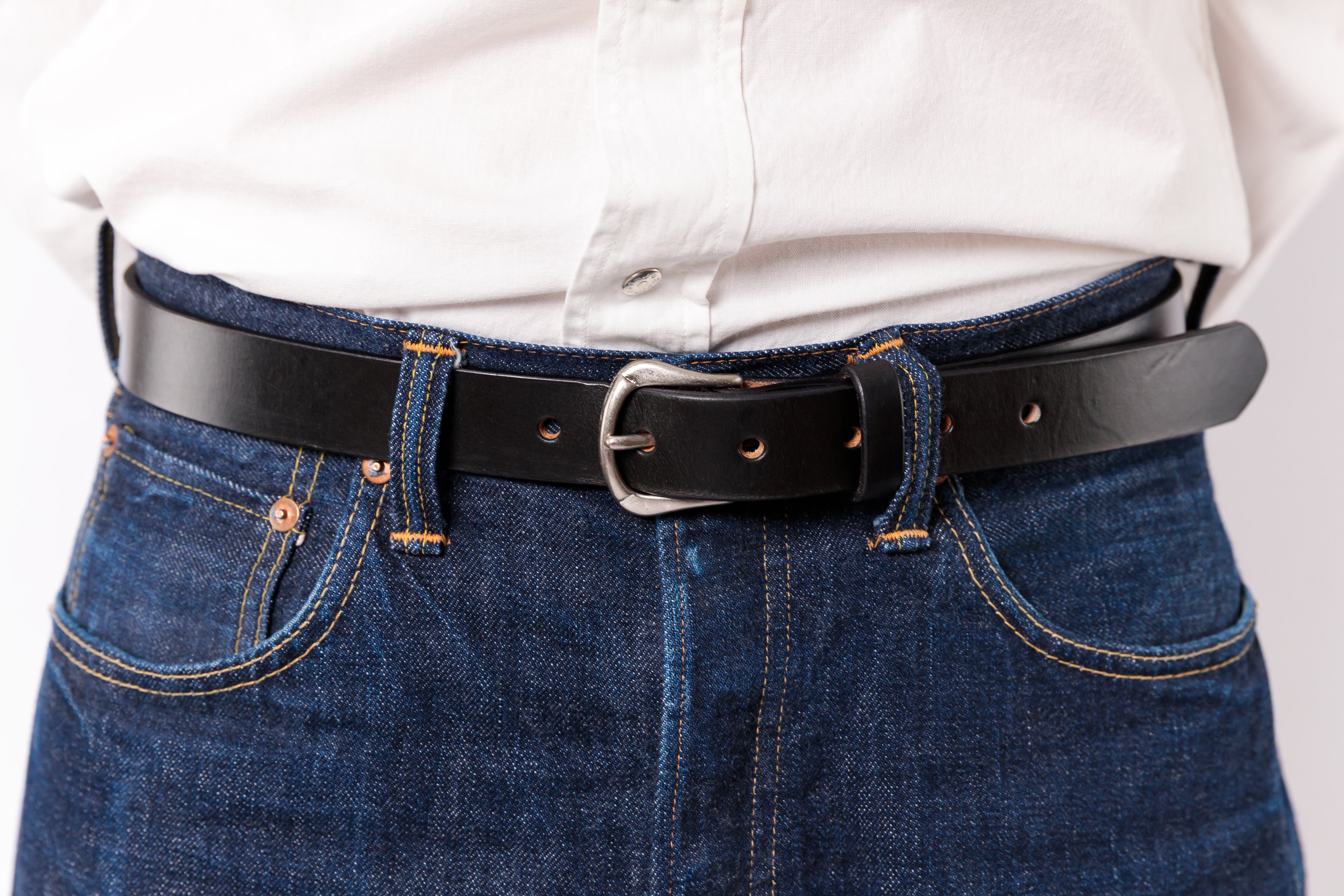 A close-up of a black leather belt with a silver buckle worn around the waist over a white shirt and blue jeans.