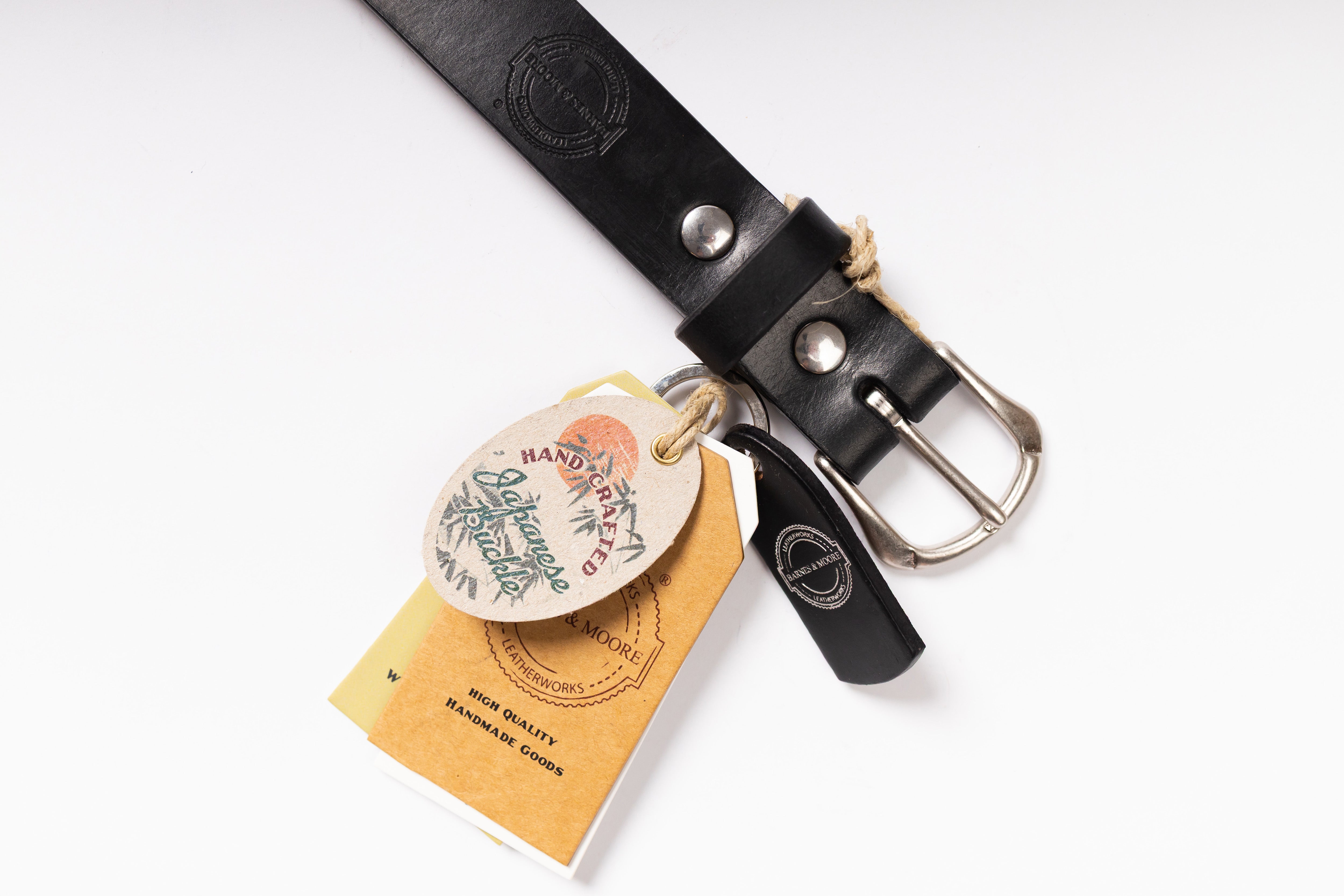 A black leather belt with a silver-tone buckle, shown on a white background with its branded hangtag and paper tag attached.