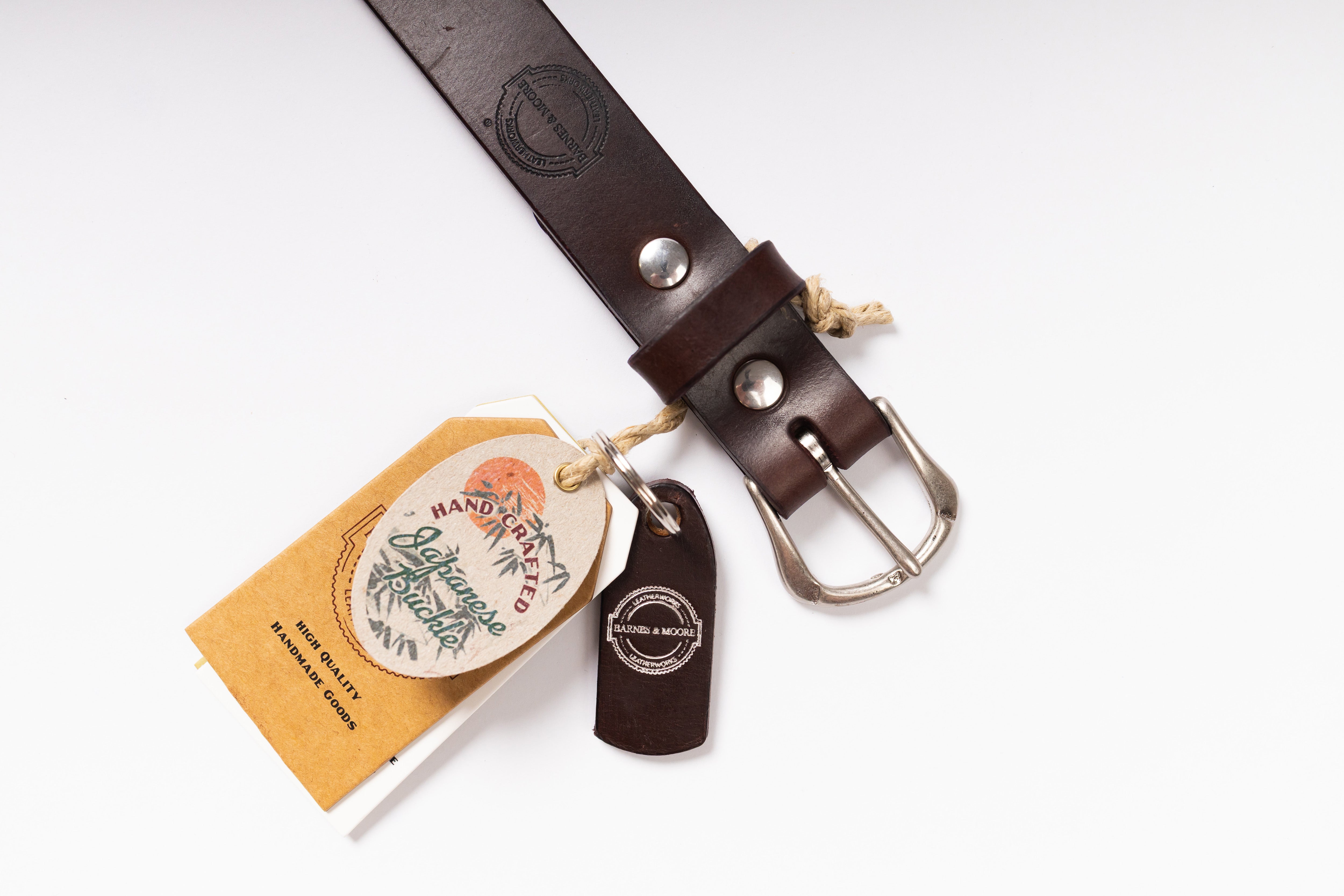 A dark brown leather belt with a silver buckle, shown with its branded paper hangtag and small leather tag on a clean white background.