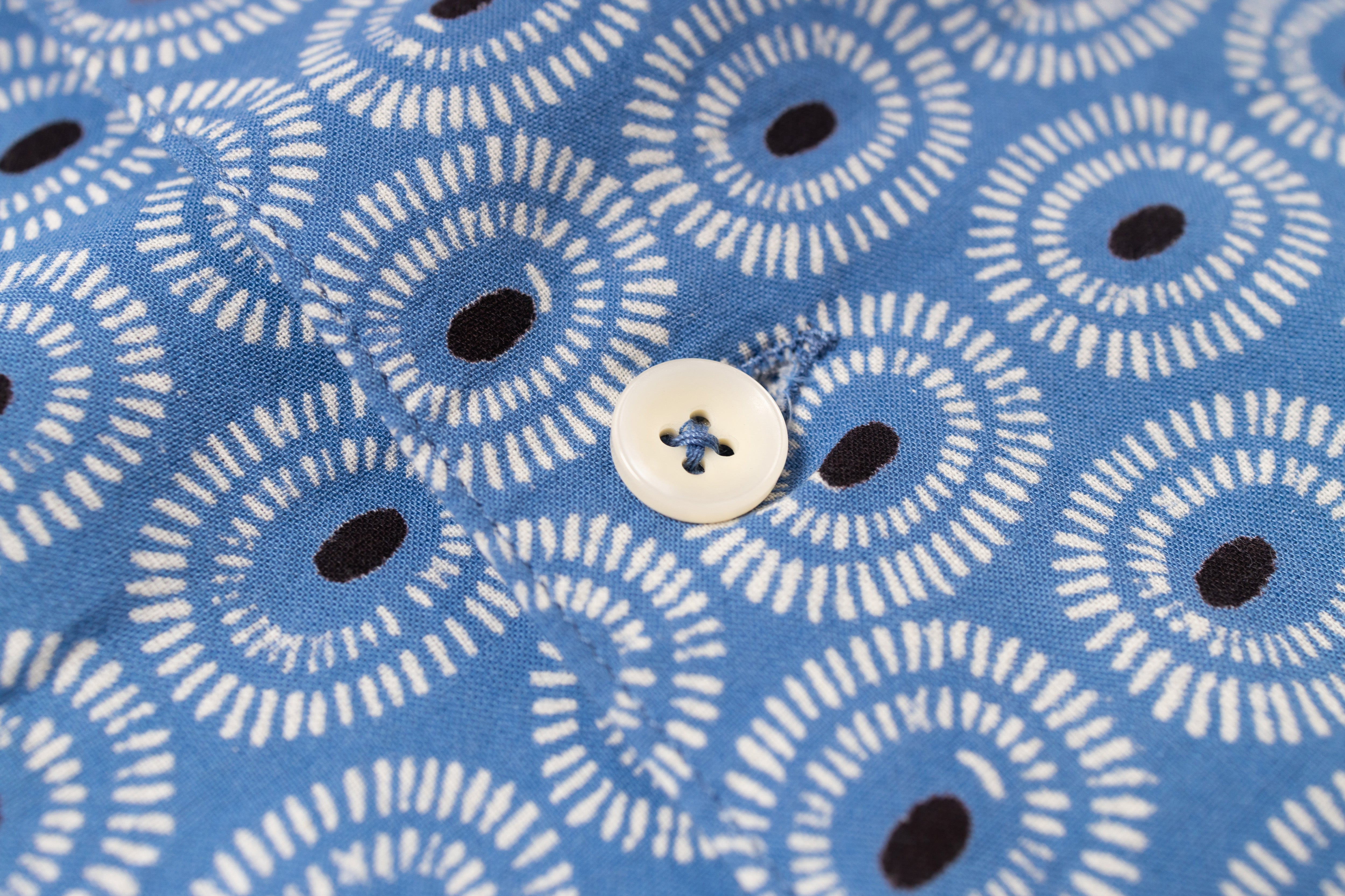 Close-up of blue fabric with white circular pattern and black dots, featuring a button.