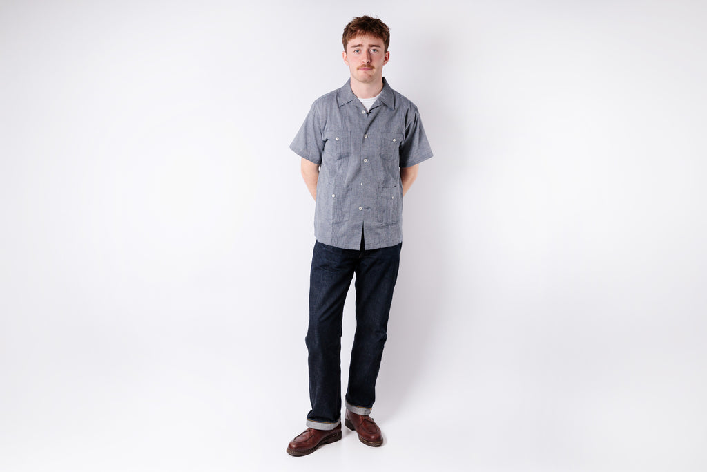Man wearing a gray checkered shirt and dark pants on a white background