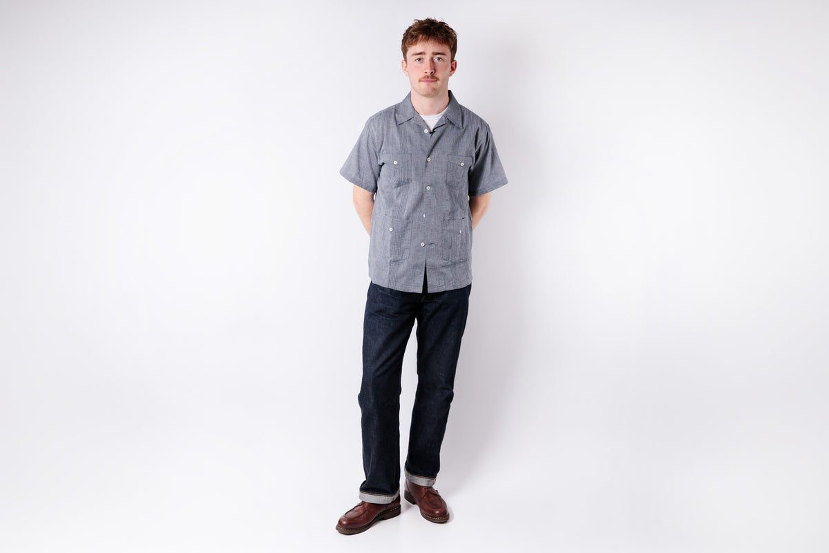 Man wearing a gray checkered shirt and dark pants on a white background