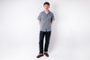 Man wearing a gray checkered shirt and dark pants on a white background