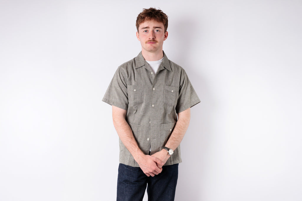 Man wearing a patterned shirt and dark pants on a white background