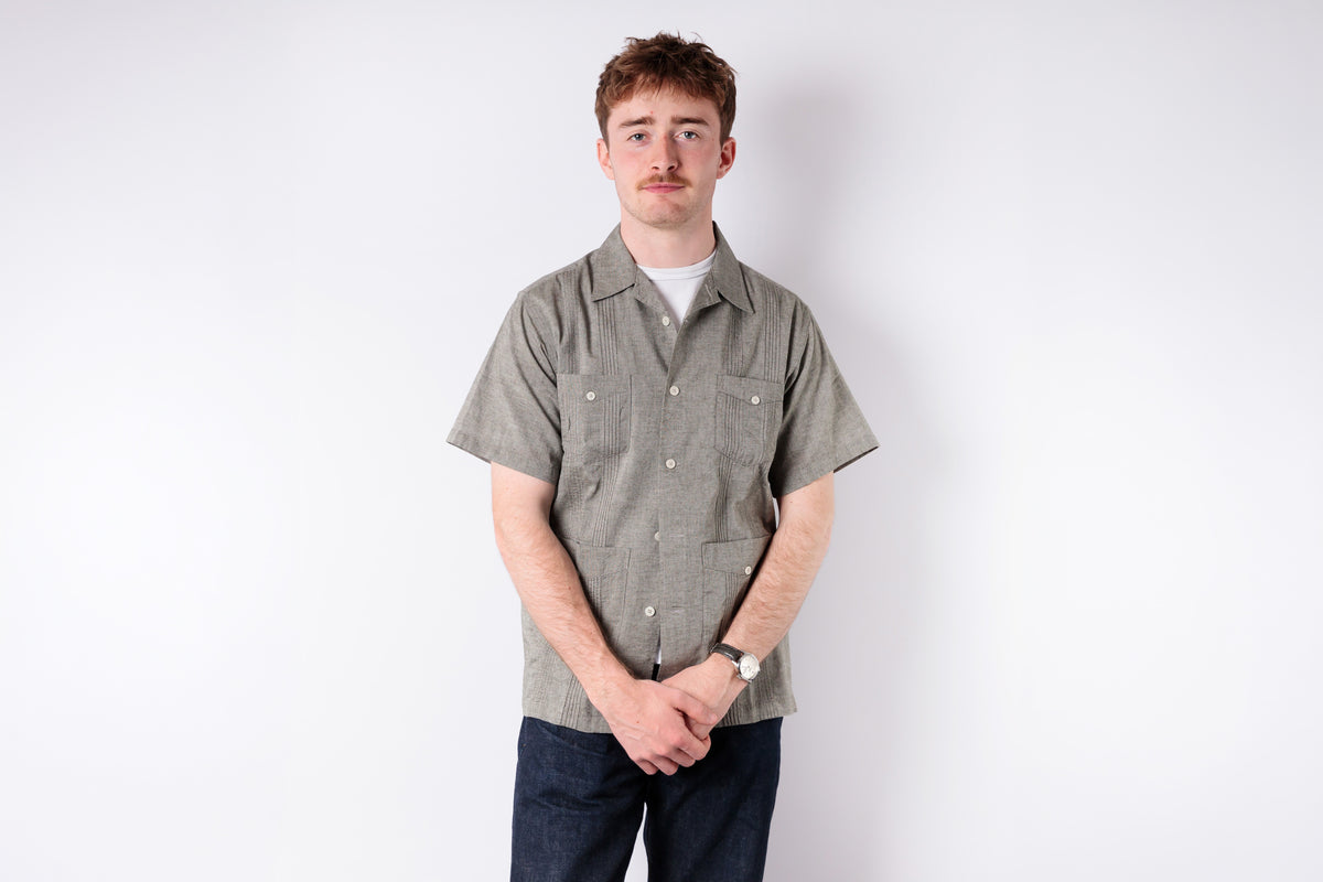 Man wearing a patterned shirt and dark pants on a white background