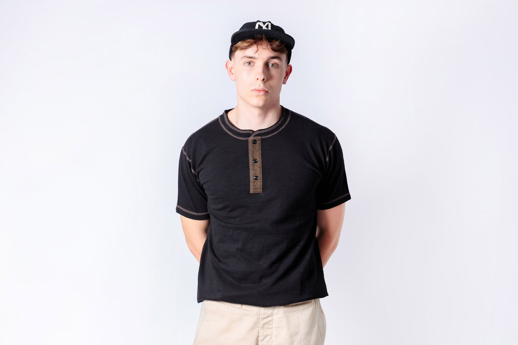 Man wearing a black shirt with brown buttons and a cap on a white background