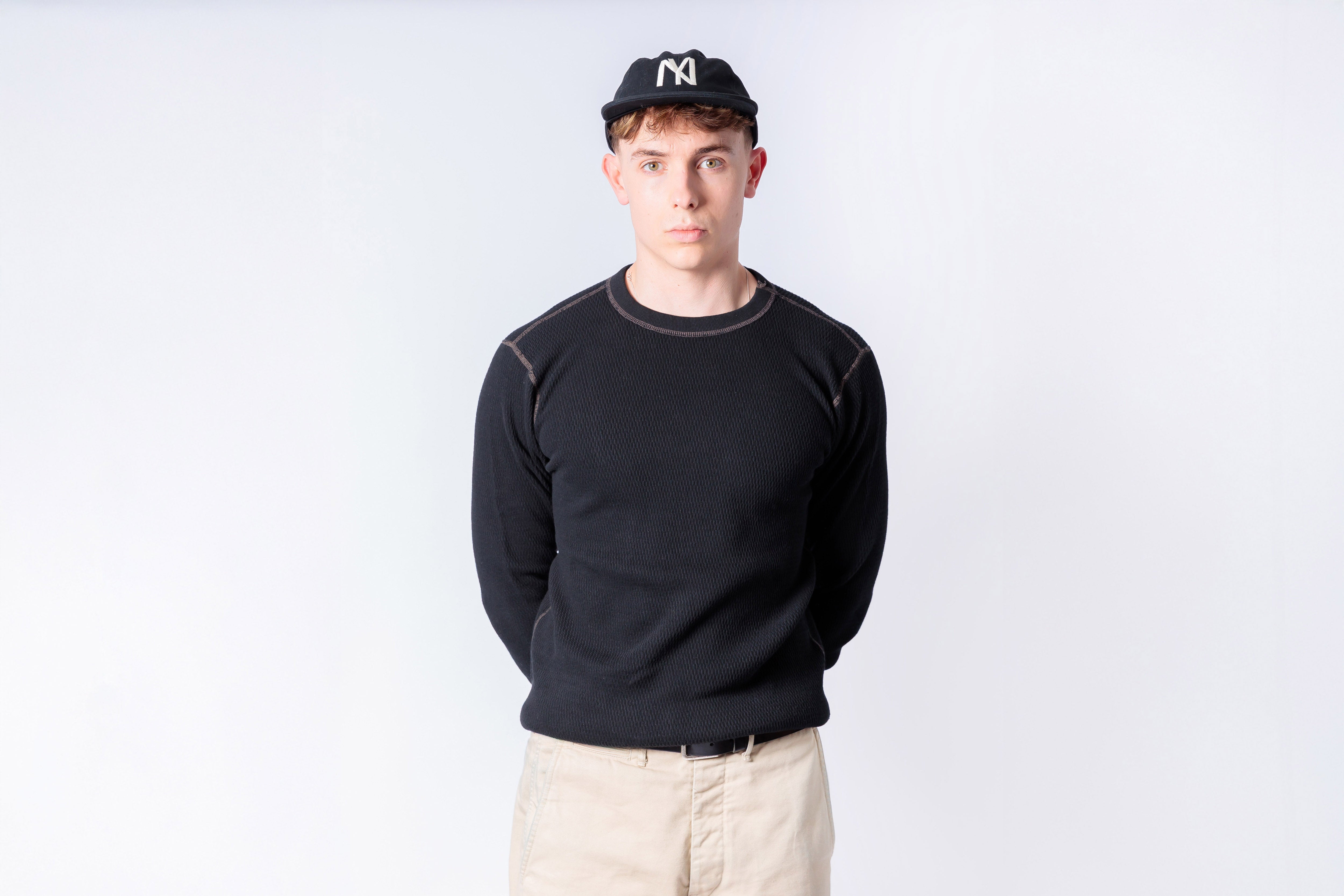 Person wearing a black sweater and beige pants against a white background
