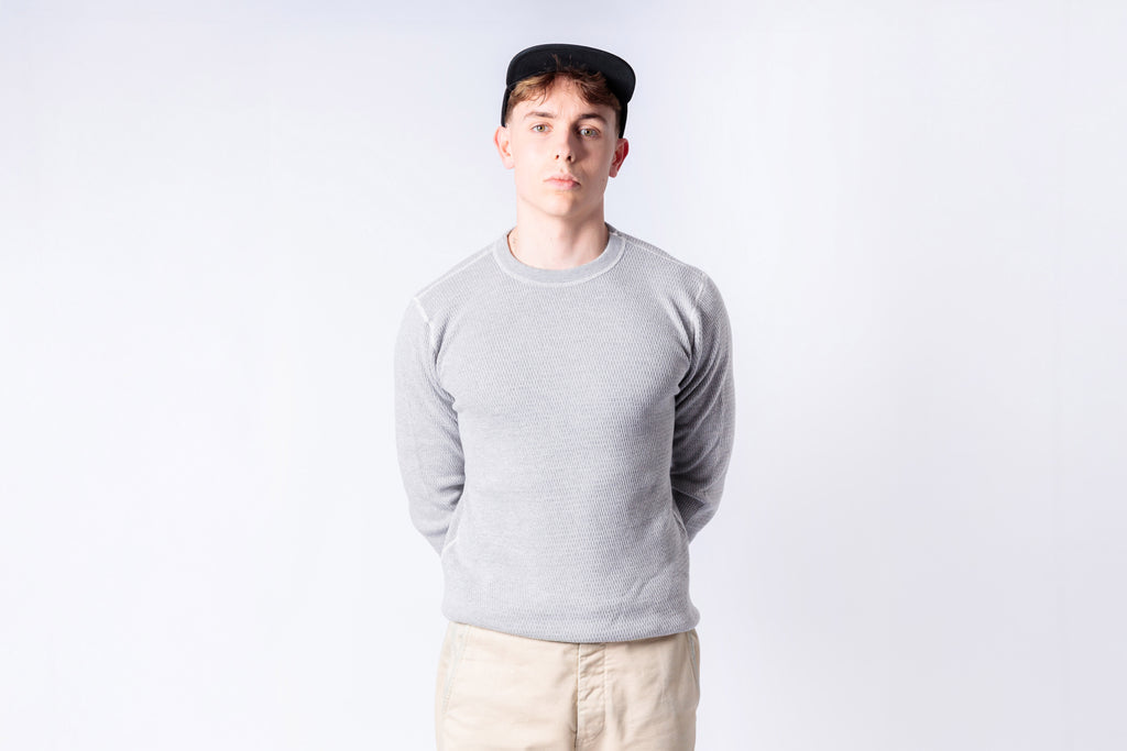 Person wearing a gray sweater and beige pants against a white background