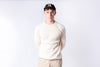 Person wearing a white sweater and beige pants with a black cap on a white background