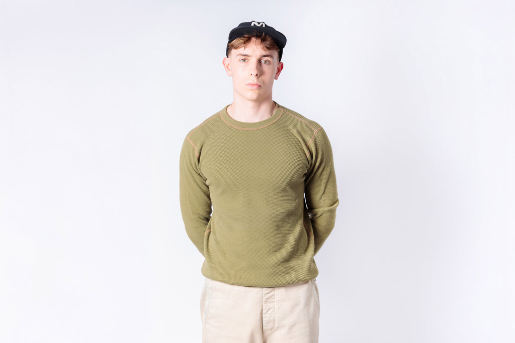 Person wearing a green sweater and beige pants on a white background