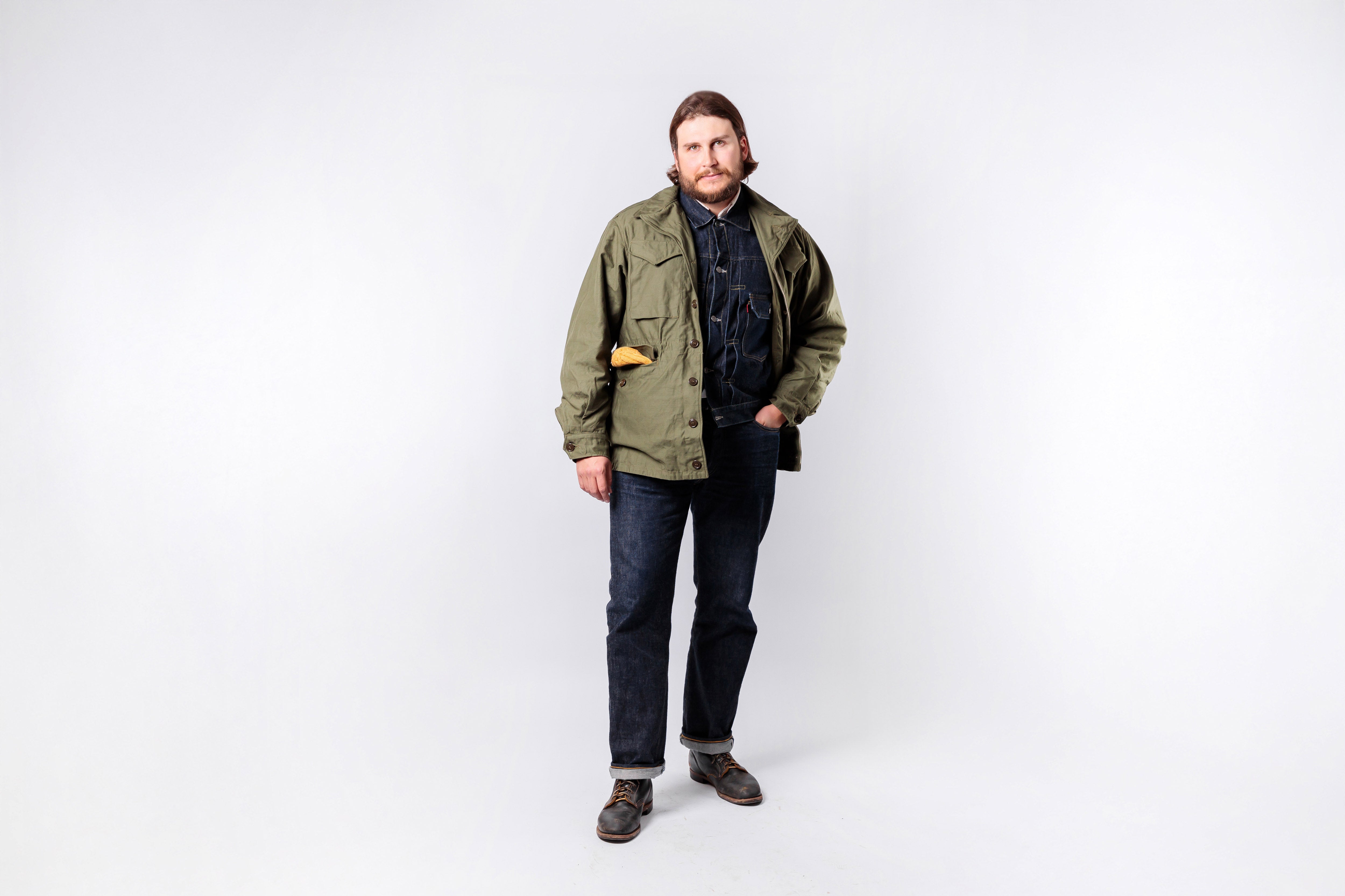Man wearing a green jacket and dark jeans on a white background