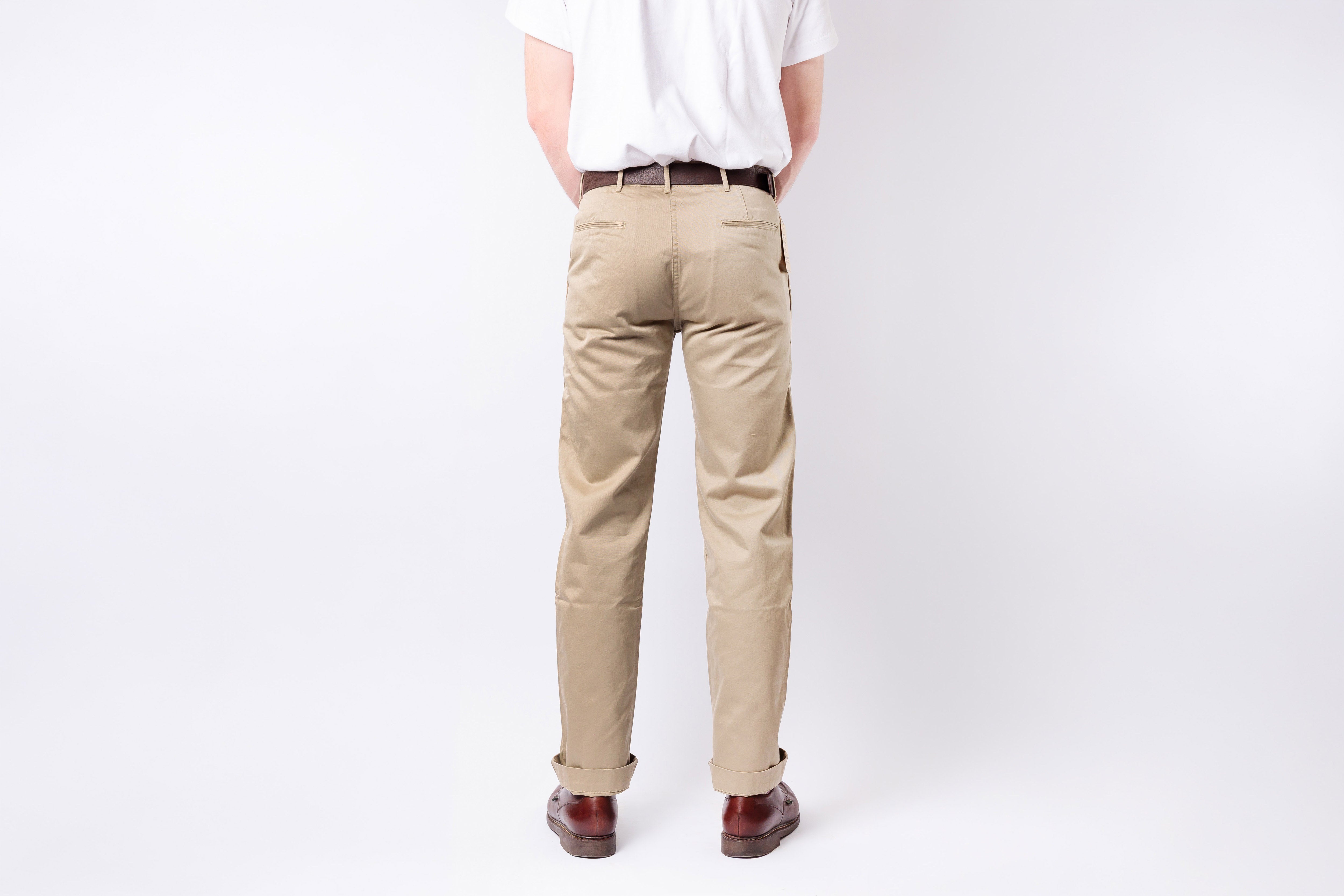 Person wearing beige pants and a white shirt on a plain background