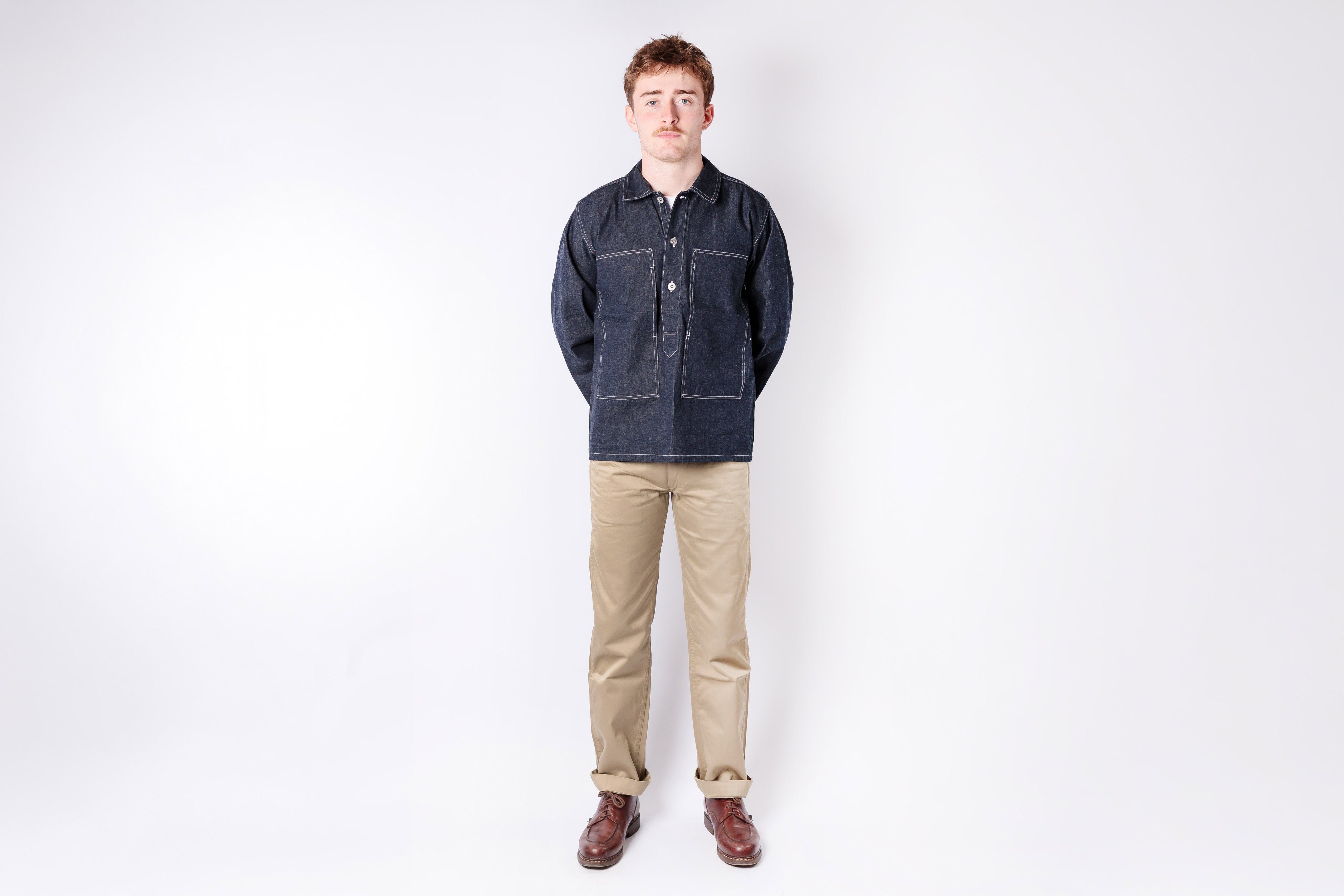 Man wearing a dark denim jacket and beige pants on a white background