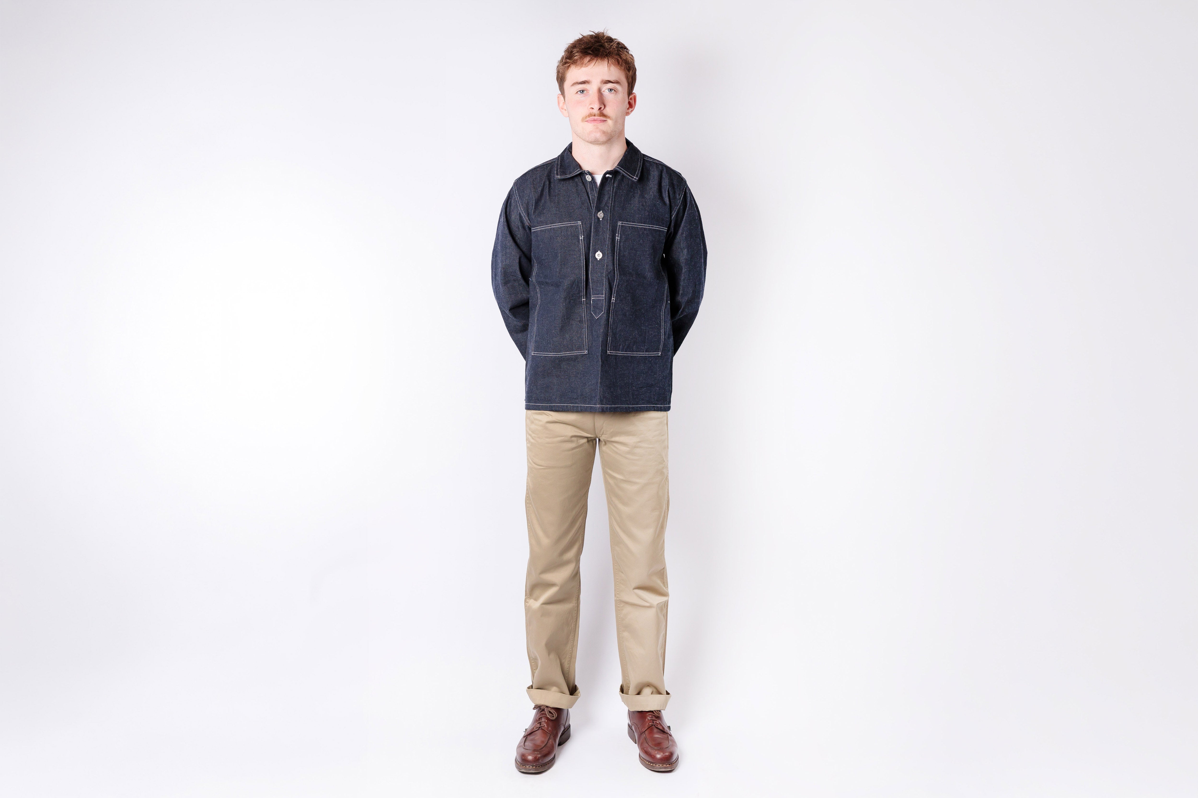 Man wearing a dark denim jacket and beige pants on a white background