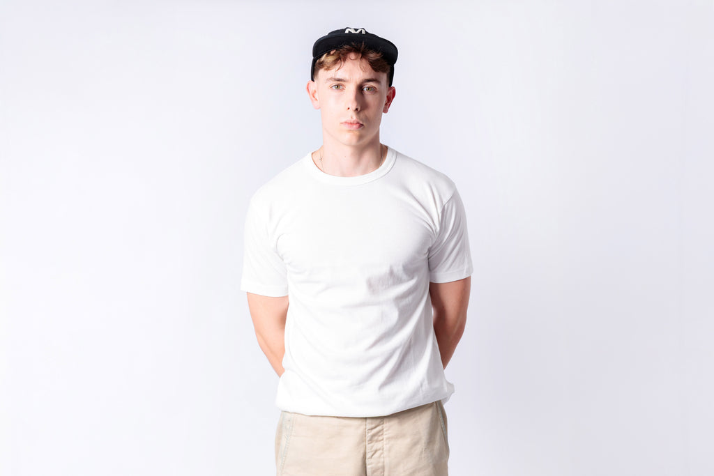 Person wearing a plain white t-shirt and beige pants against a light gray background
