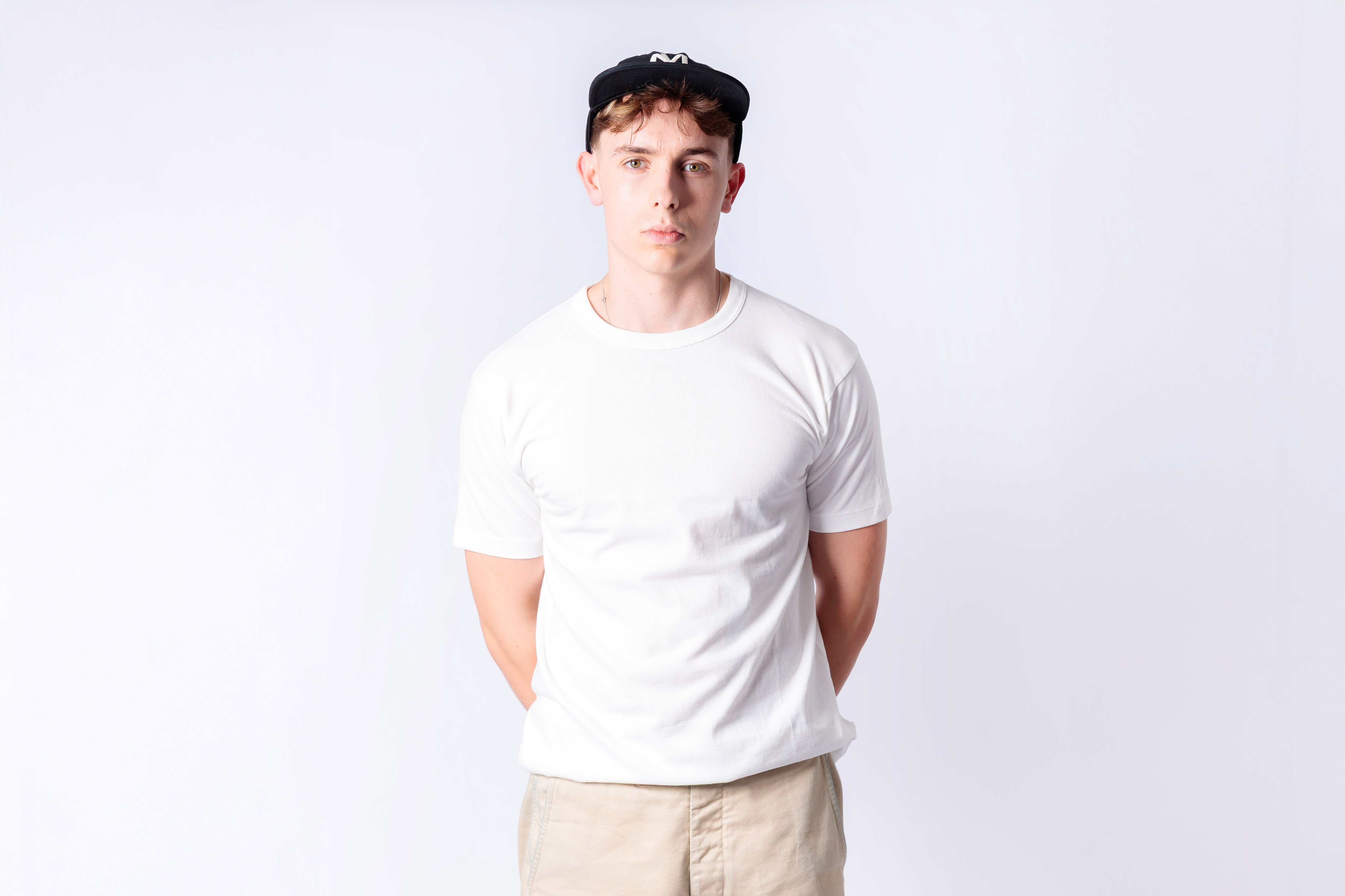 Person wearing a plain white t-shirt and beige pants against a light gray background