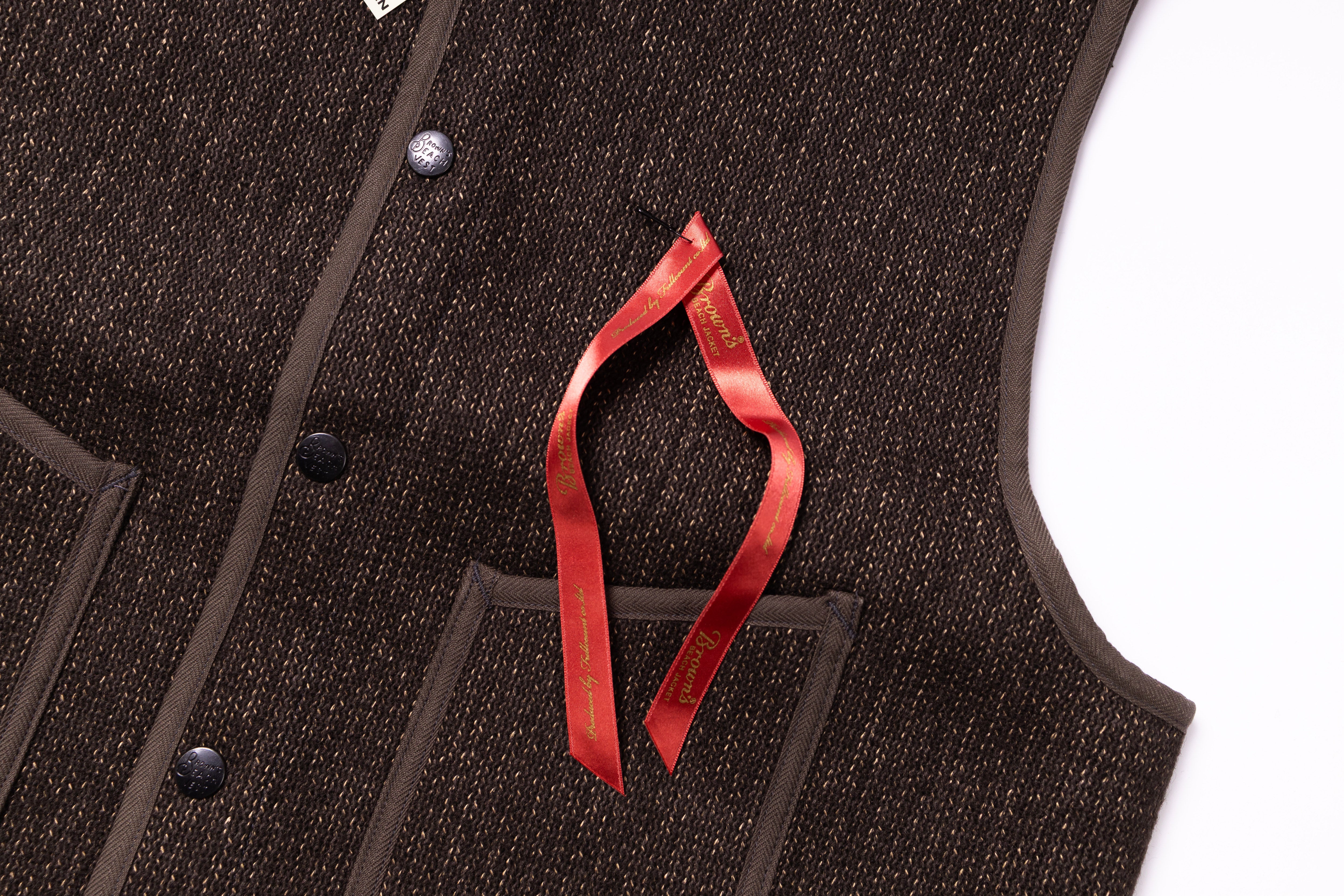 Close-up of a brown textured vest with a red ribbon and button details.