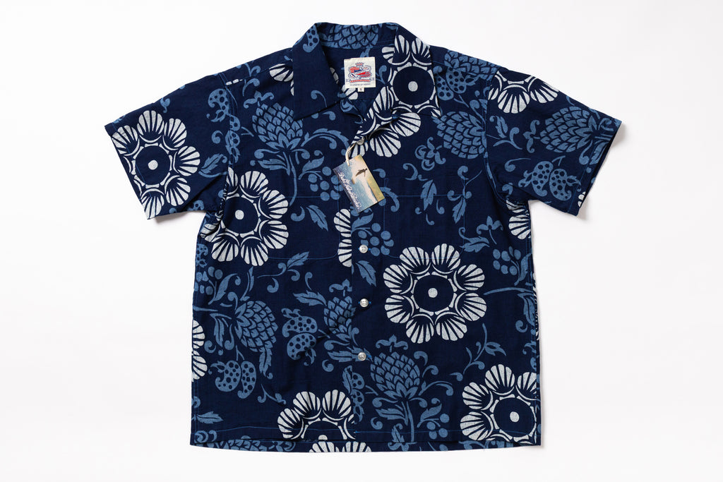A short-sleeve button-up camp shirt in navy blue with a white floral and pinecone pattern, shown flat against a white background with retail tags attached.