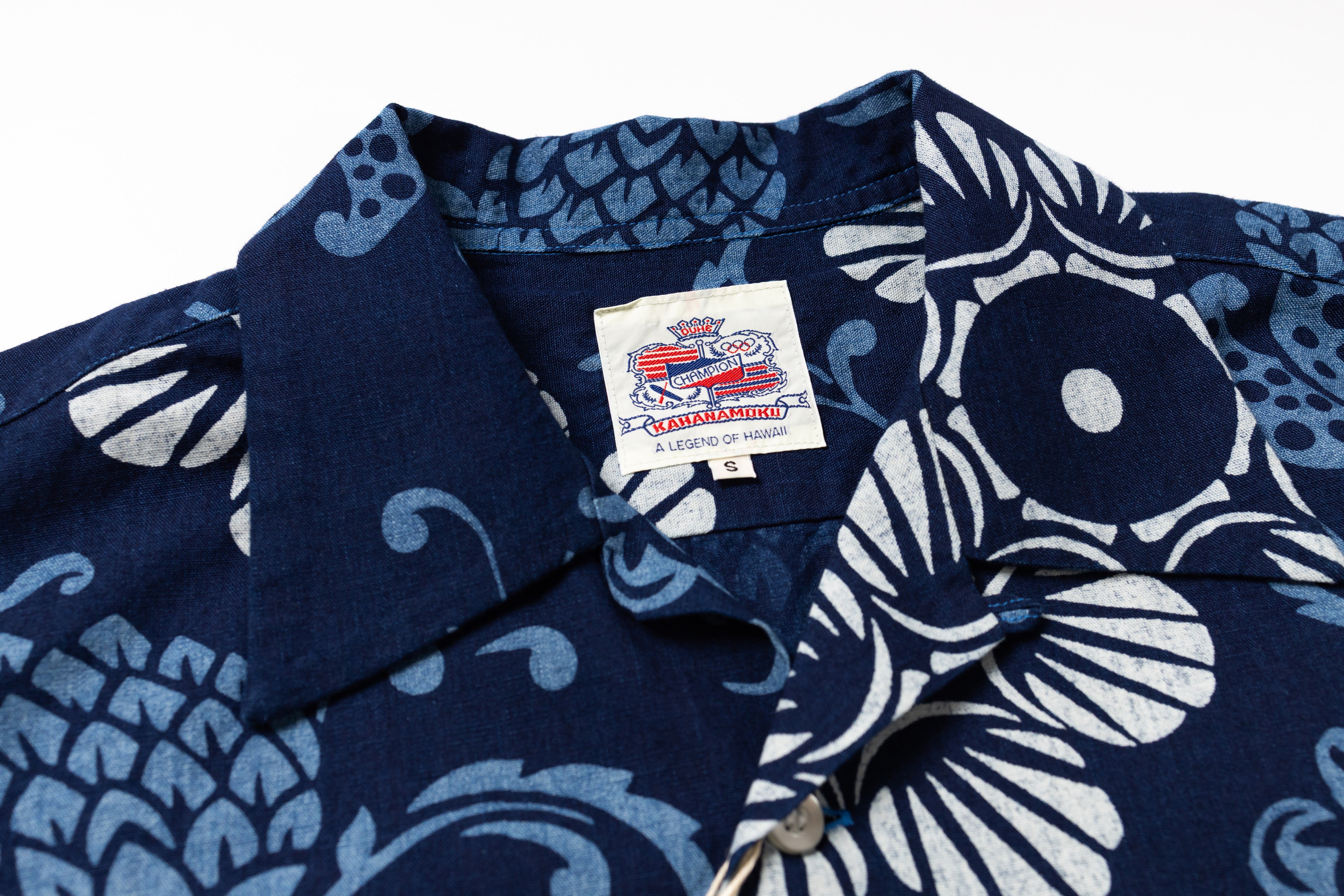 Close-up of a short-sleeve button-up shirt with a navy blue base and a white floral and wave pattern. 