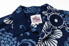 Close-up of a short-sleeve button-up shirt with a navy blue base and a white floral and wave pattern. 