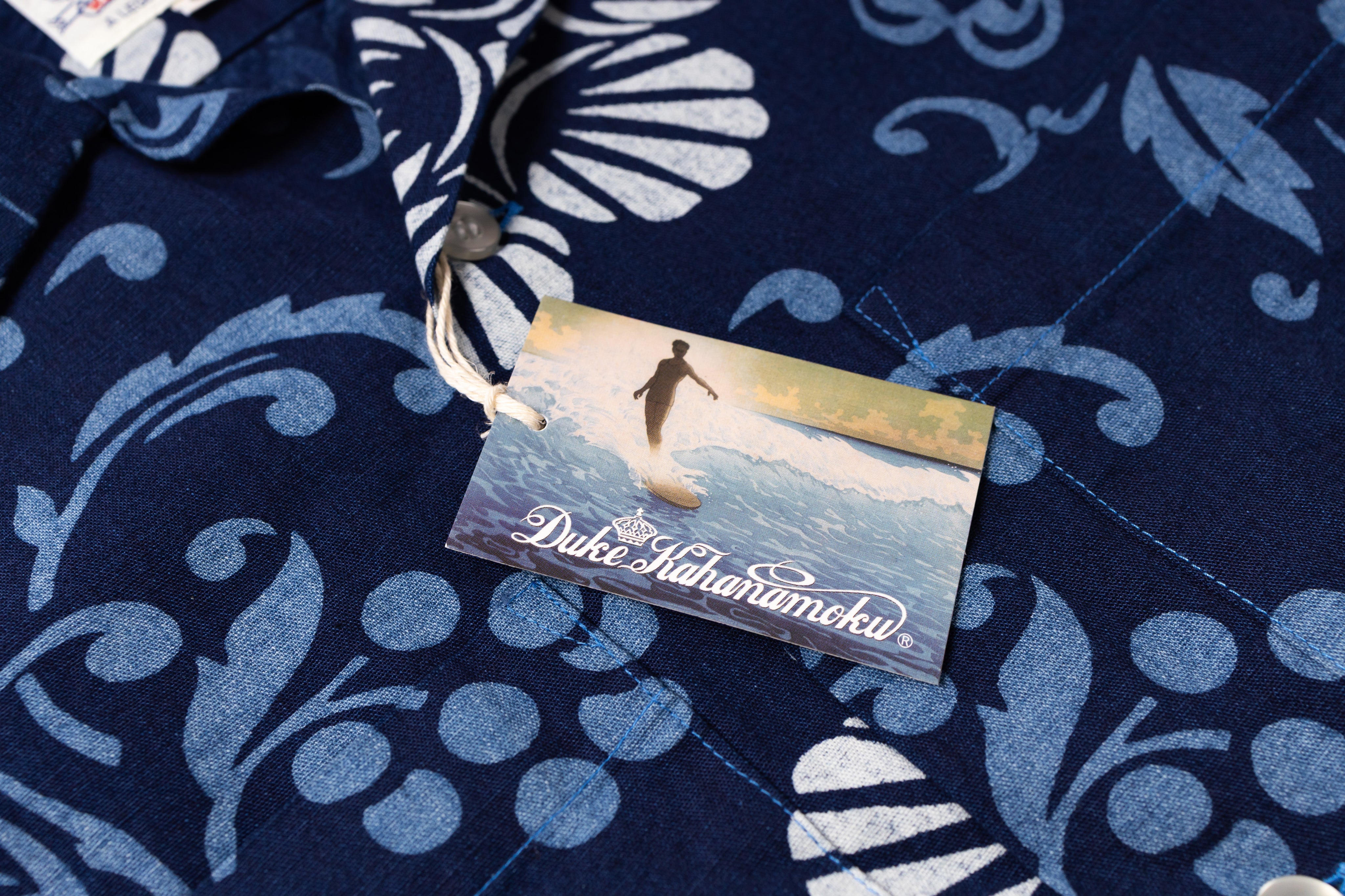 Close-up of a navy blue patterned shirt with a visible fabric tag wtih small surfing illustration on the tag.