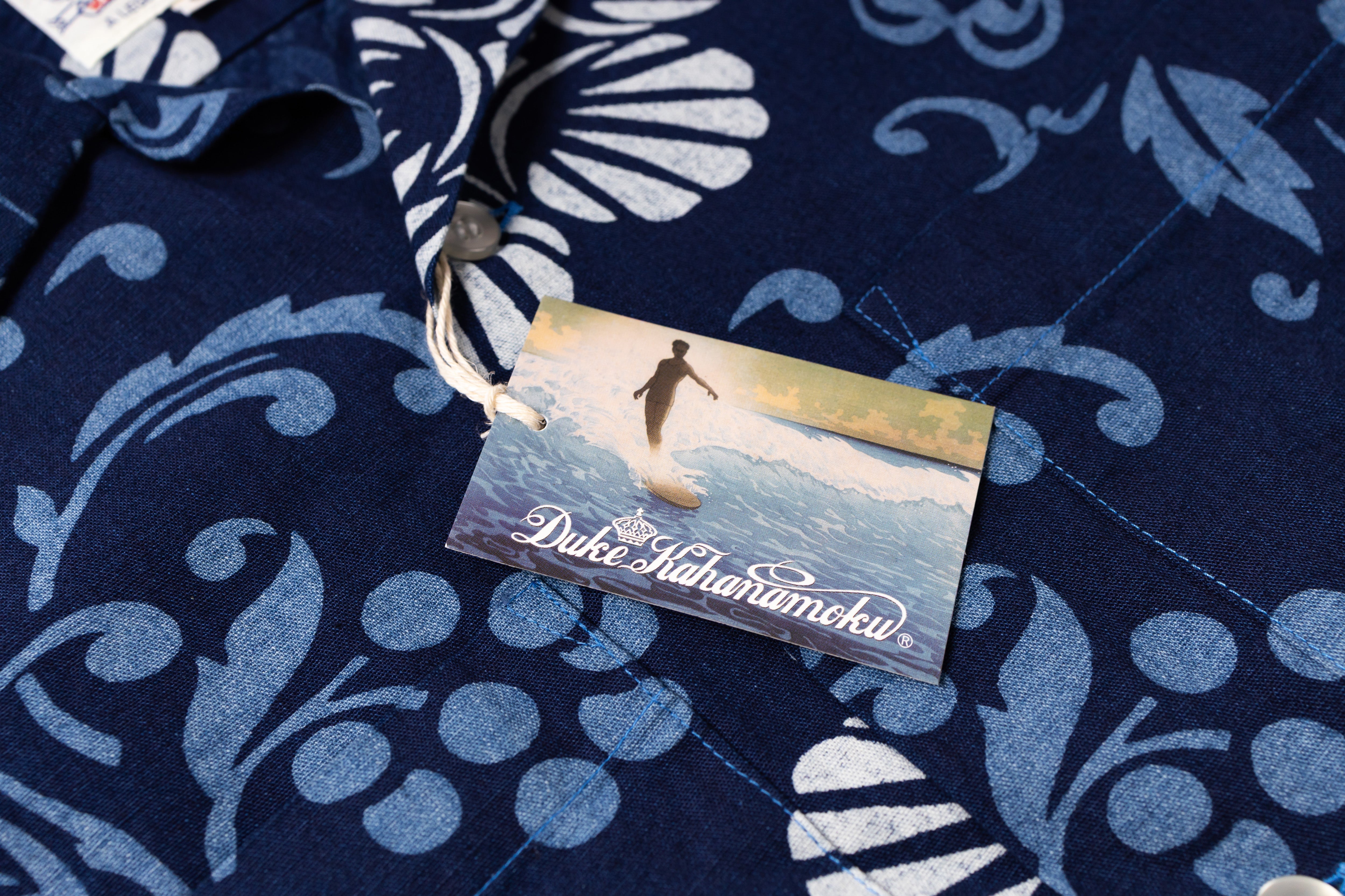 Close-up of a navy blue patterned shirt with a visible fabric tag wtih small surfing illustration on the tag.