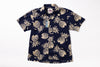 A short-sleeve button-up camp shirt with a navy blue base and a beige pineapple pattern, shown flat against a white background with a hangtag attached.