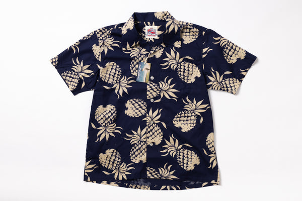 A short-sleeve button-up camp shirt with a navy blue base and a beige pineapple pattern, shown flat against a white background with a hangtag attached.