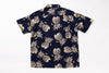 A short-sleeve button-up shirt with an all-over beige pineapple print on a dark navy blue background, laid flat against a white background.